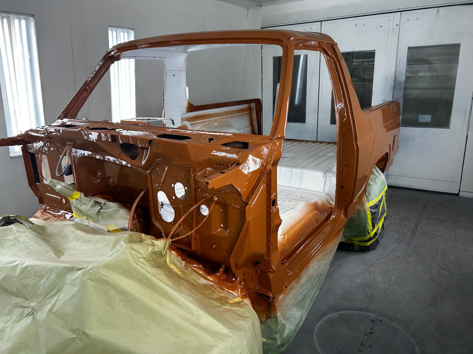 Brown classic truck frame being painted in a spray booth.