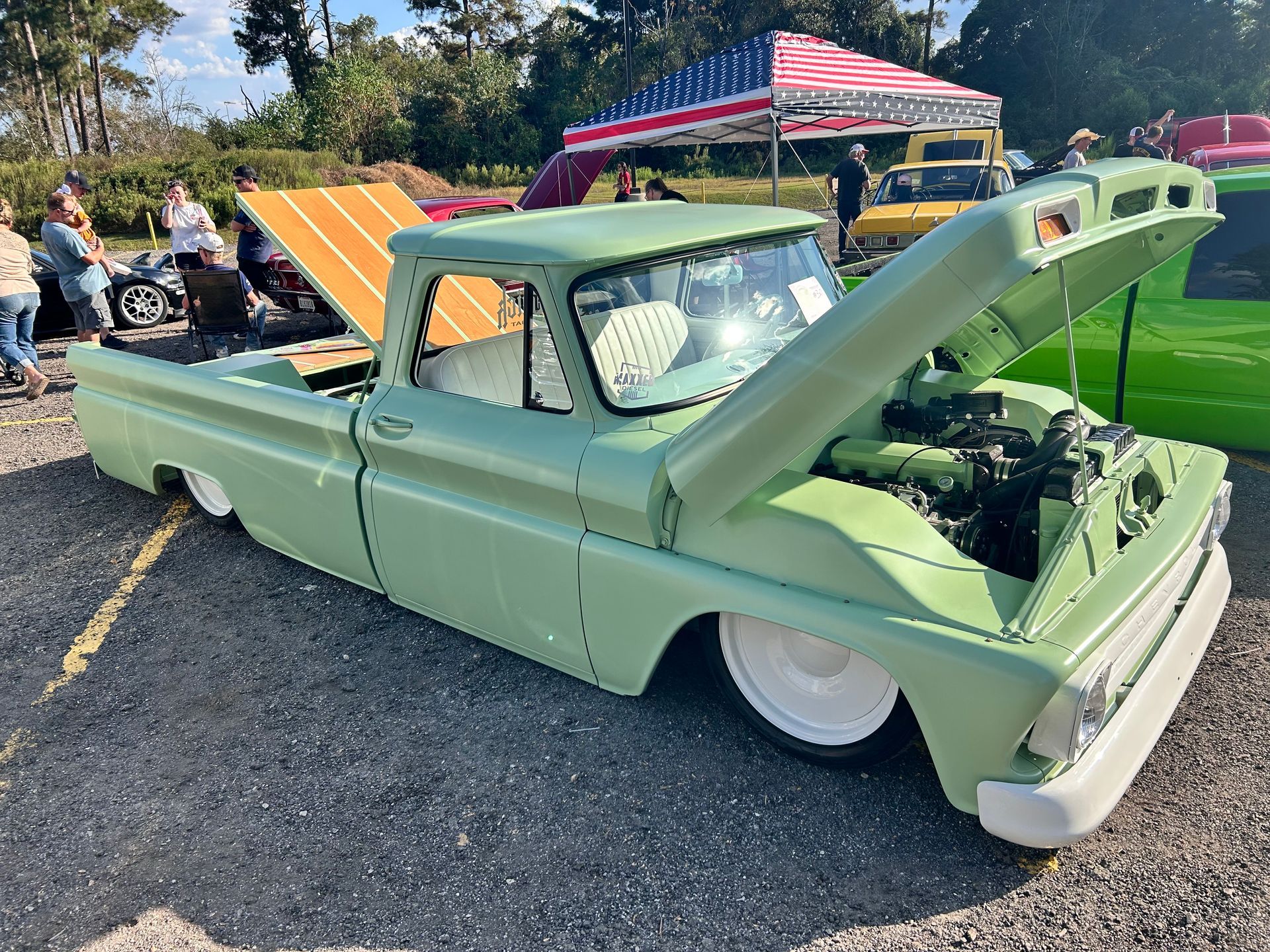 Green vintage pickup truck with the hood open, at a car show.