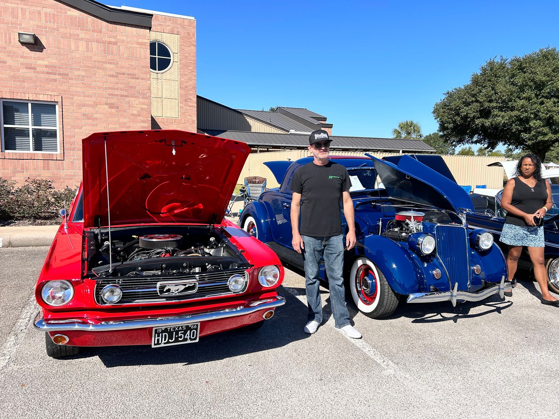 A red Mustang and blue Ford, with open hoods, at a car show; people stand nearby.