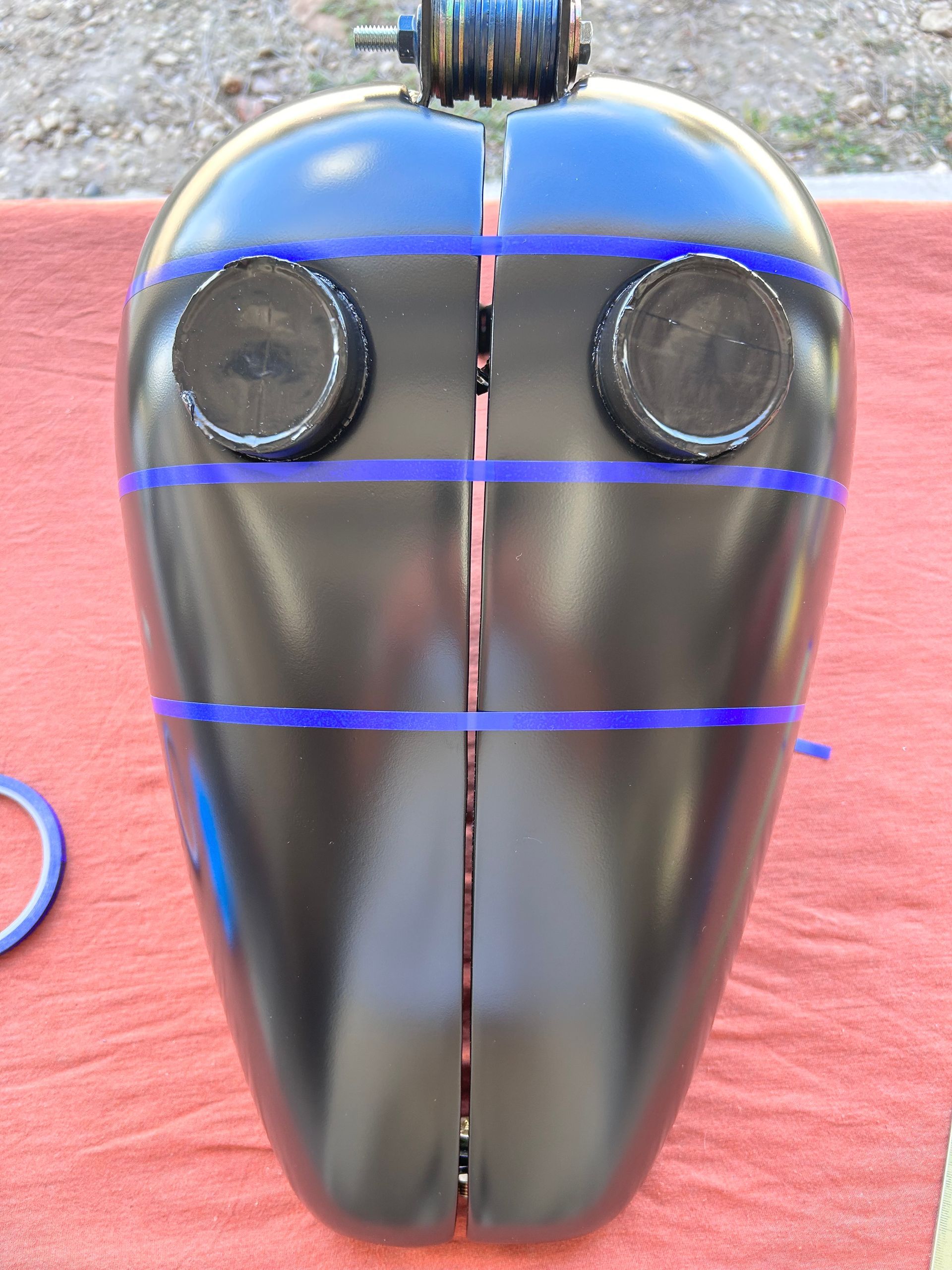 Black motorcycle gas tank, blue pinstripes, two halves, caps at top.
