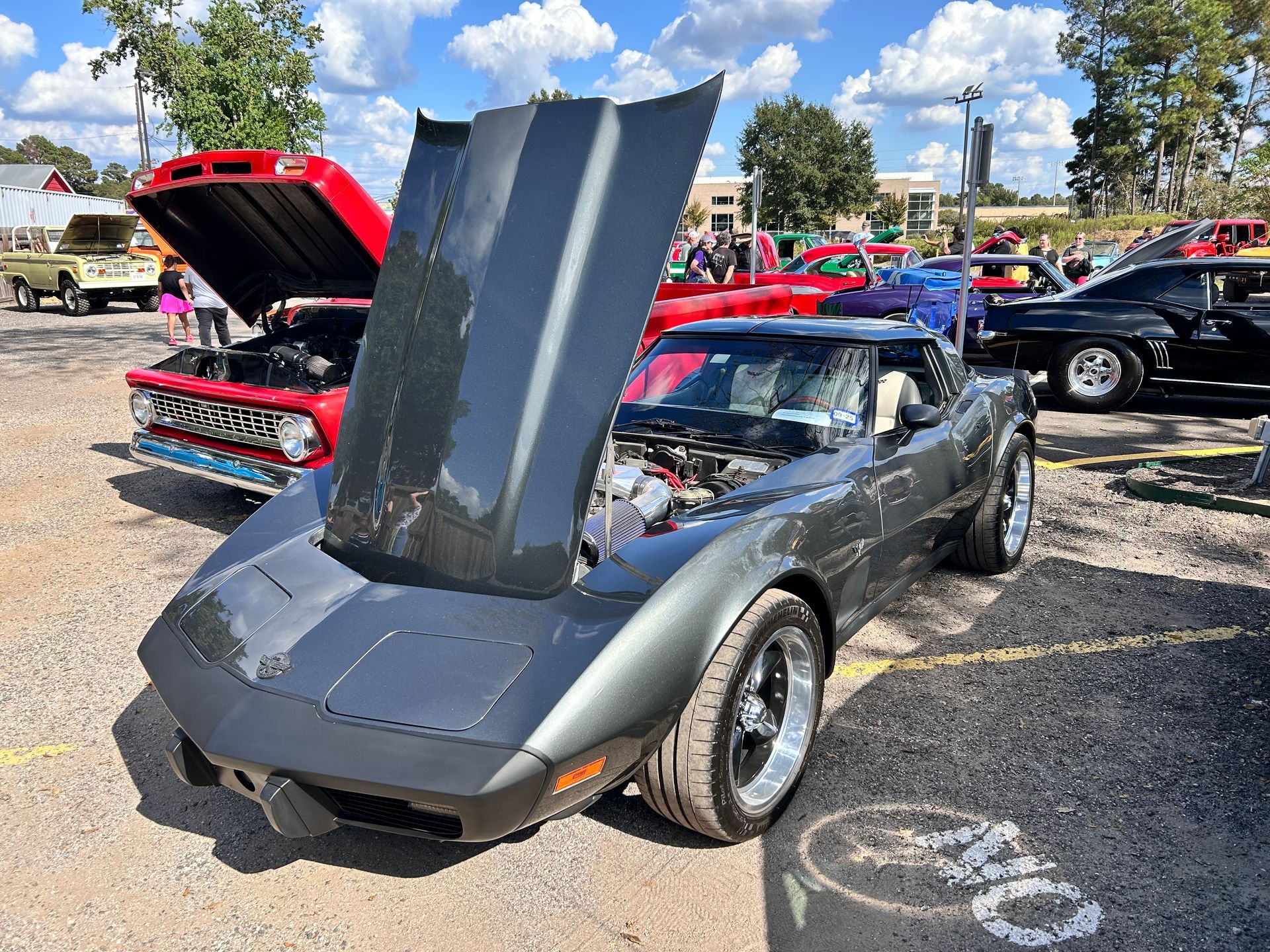 Dark grey classic Corvette with open hood at car show.