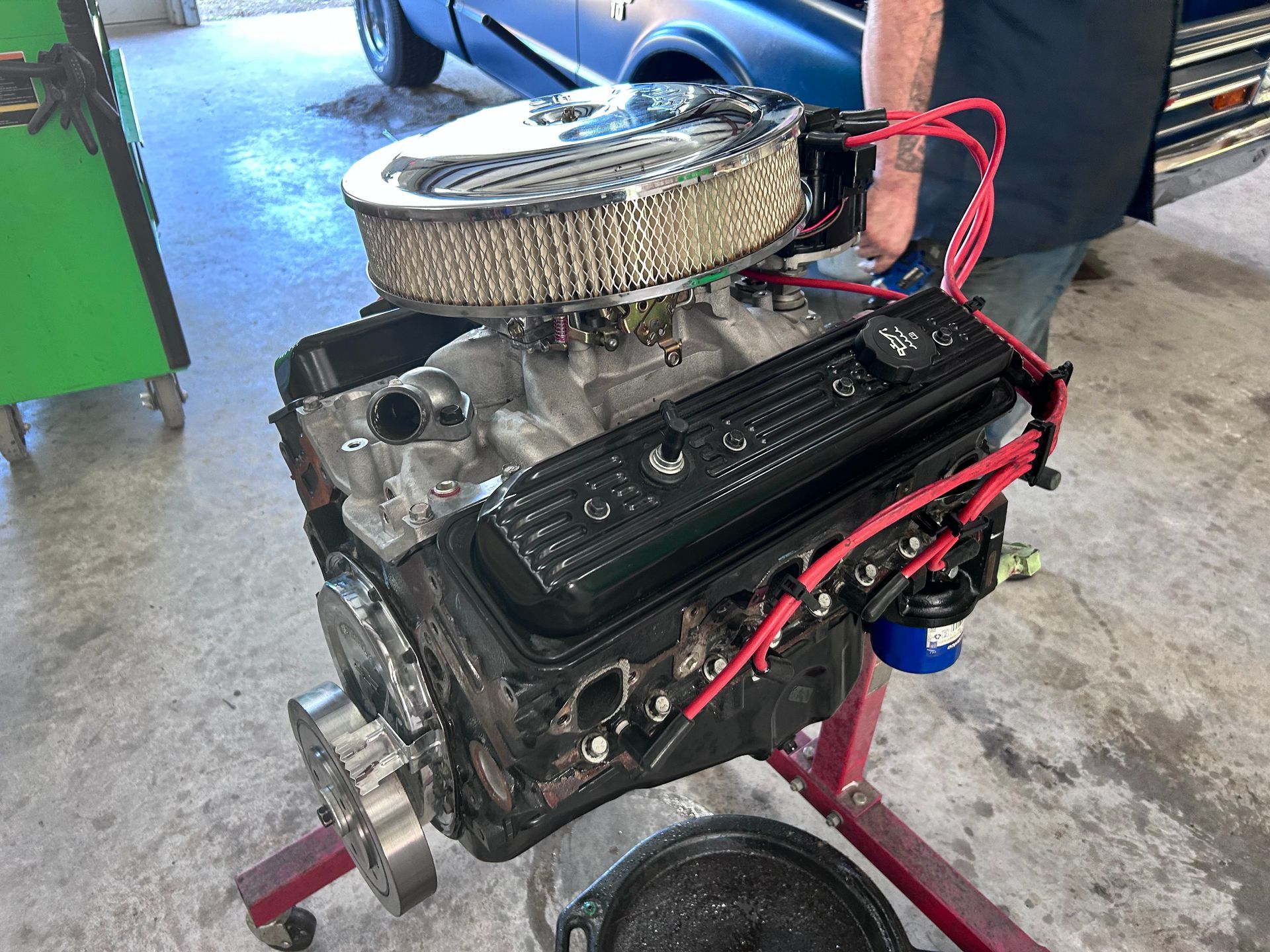 Engine on a red stand, with air filter, red spark plug wires, and black valve covers, in a garage.