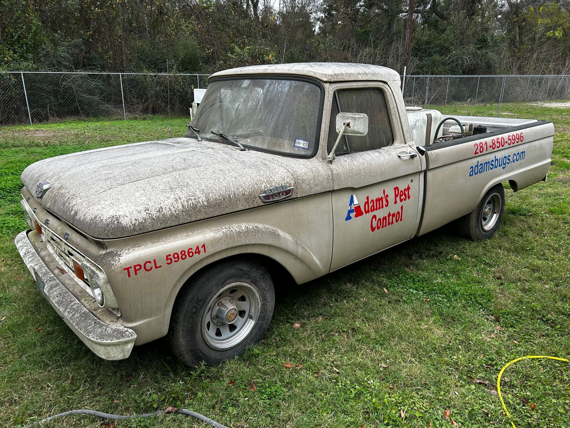 Tan, vintage Ford pickup truck in a grassy yard with business name on the side.