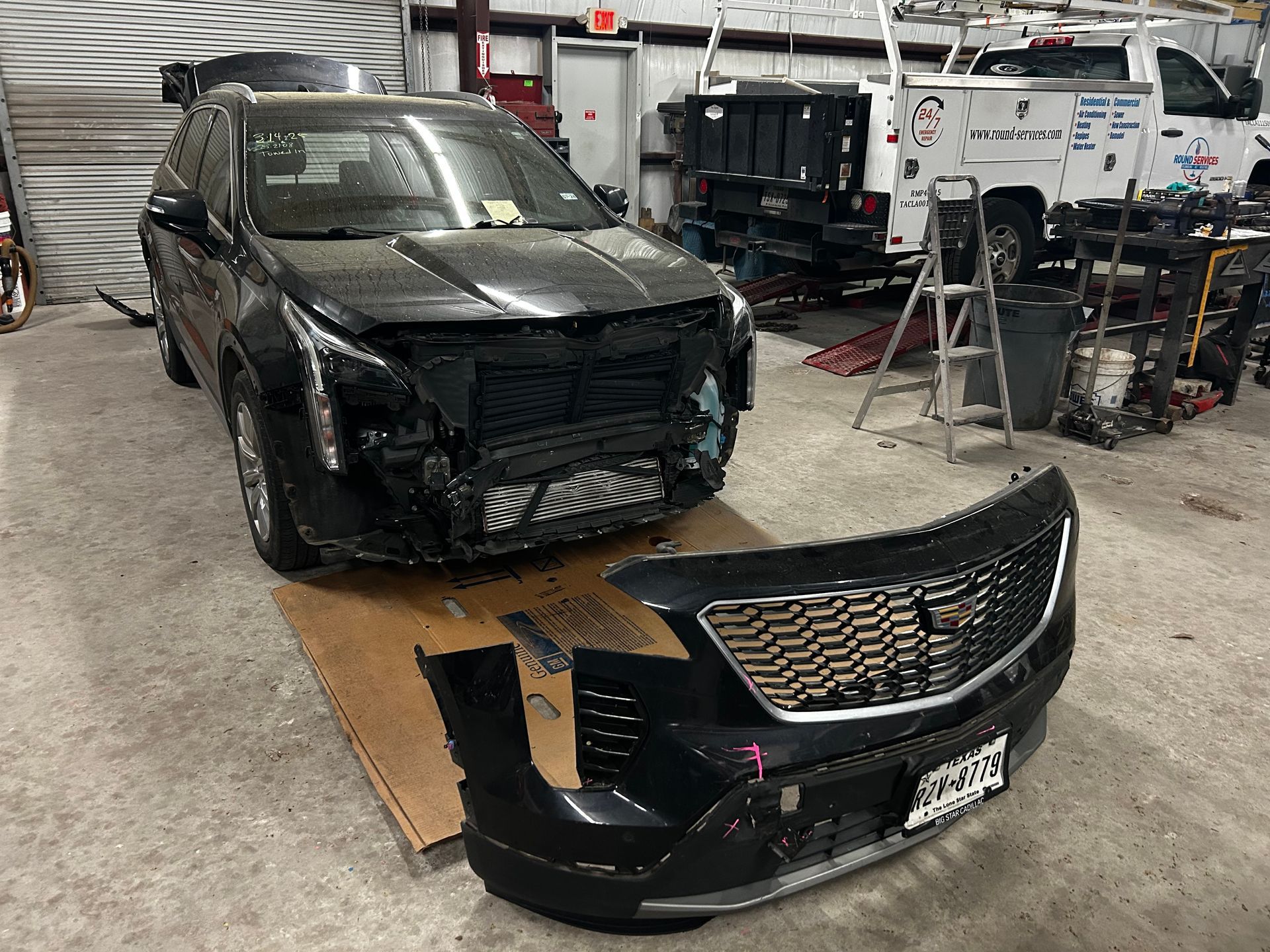 Black SUV with front end damage, bumper removed in repair shop.
