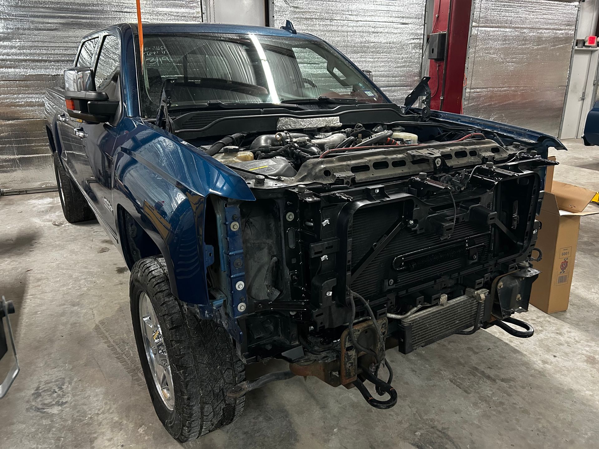 Blue pickup truck, front end disassembled, in a repair shop.