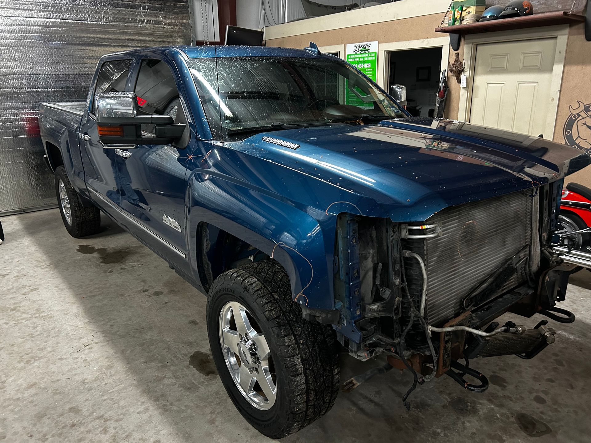 Blue pickup truck with front-end damage, parked in a garage or workshop.