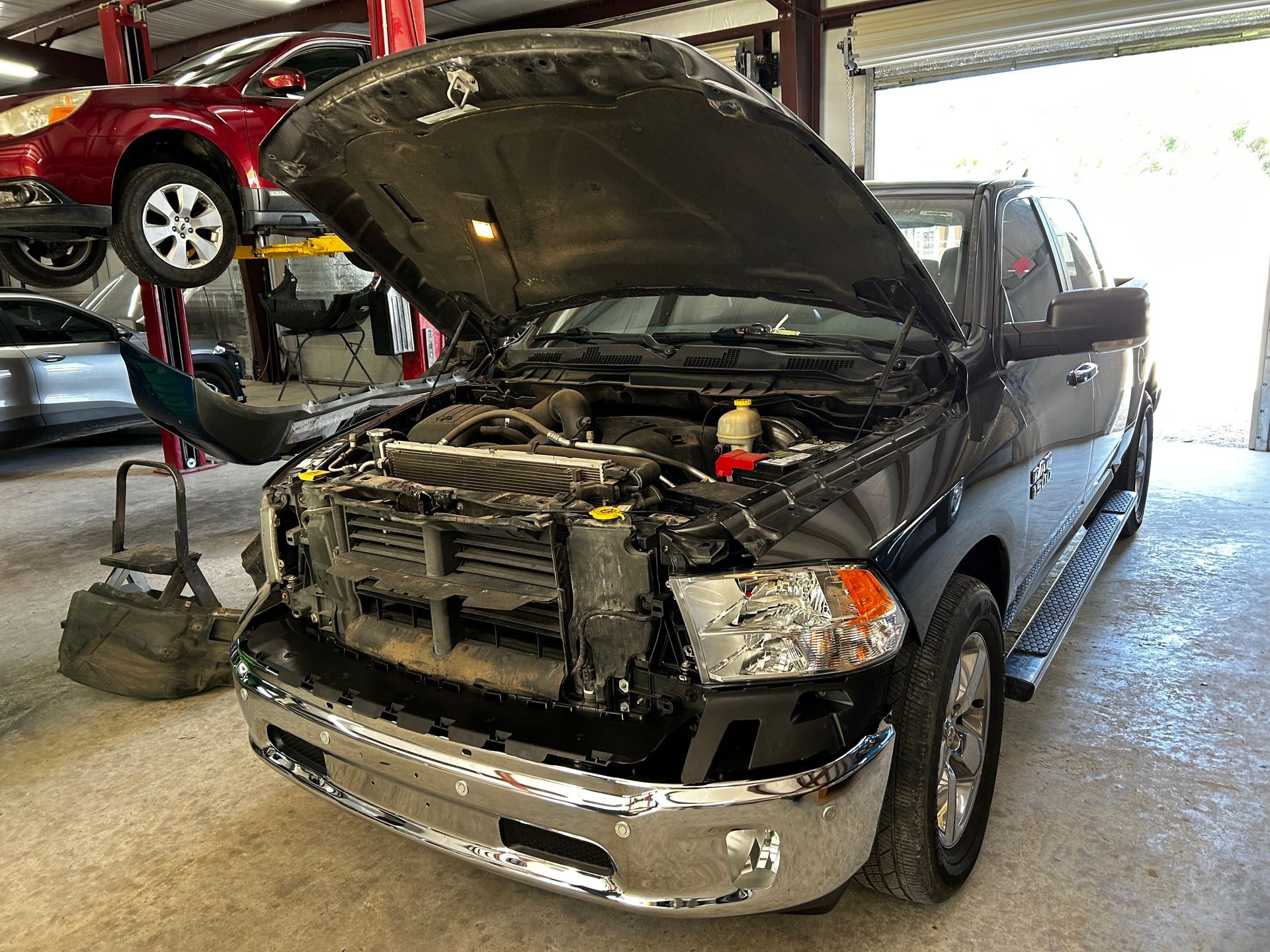Black pickup truck with open hood in a garage. Another car is on a lift in the background.