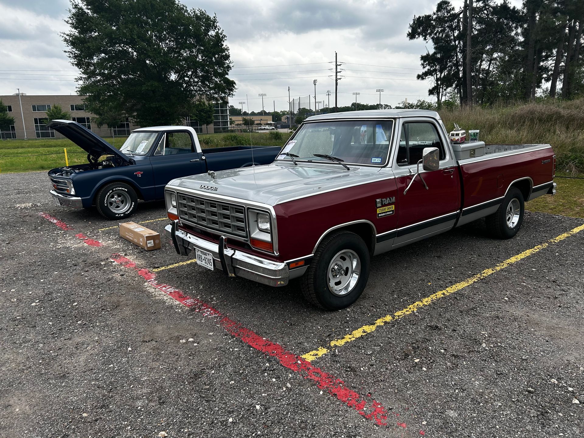 Two classic pickup trucks parked outdoors; one blue, one red and silver, on gravel.