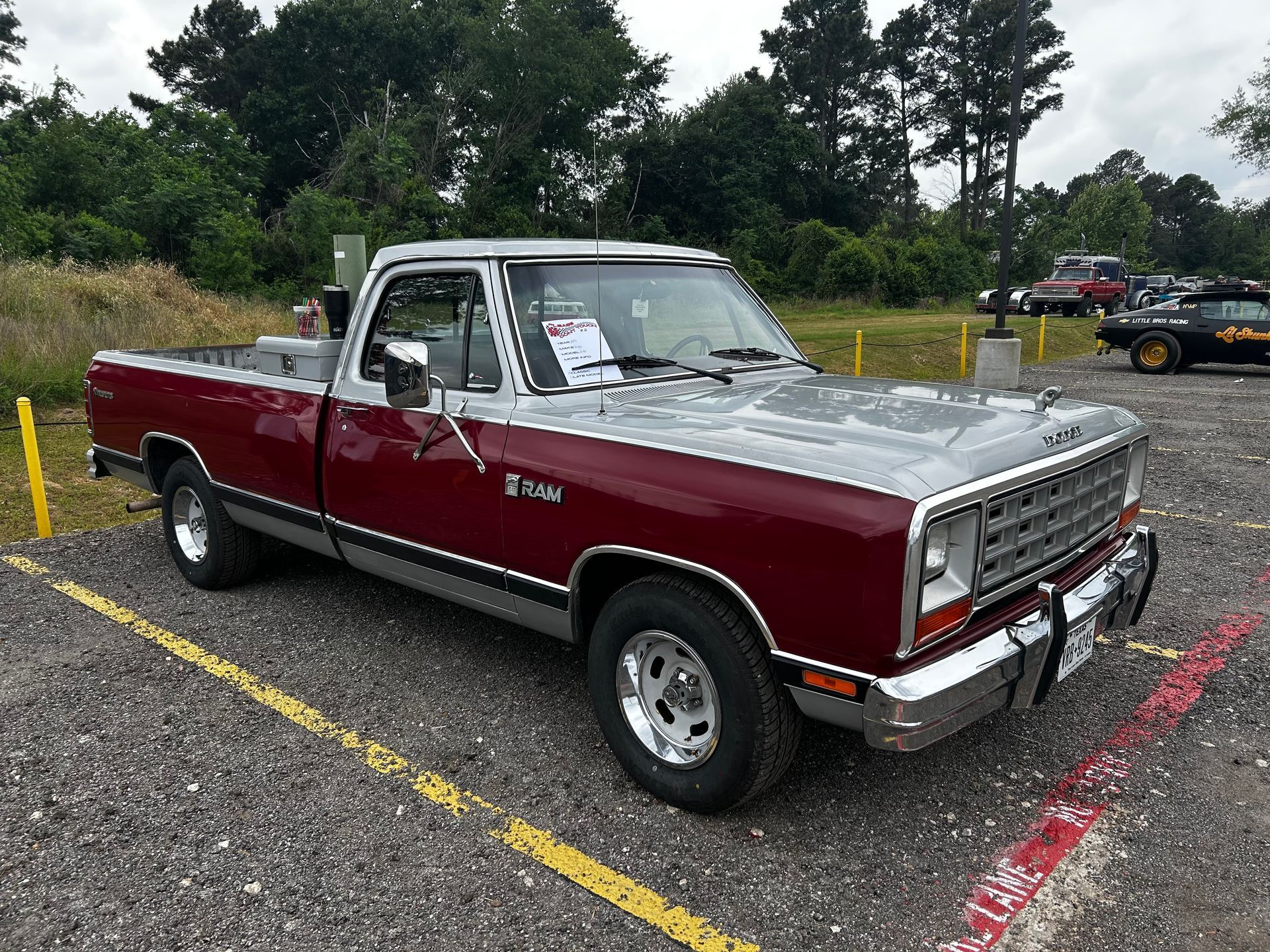Classic red and silver Dodge Ram pickup truck parked in a gravel lot at a car show.