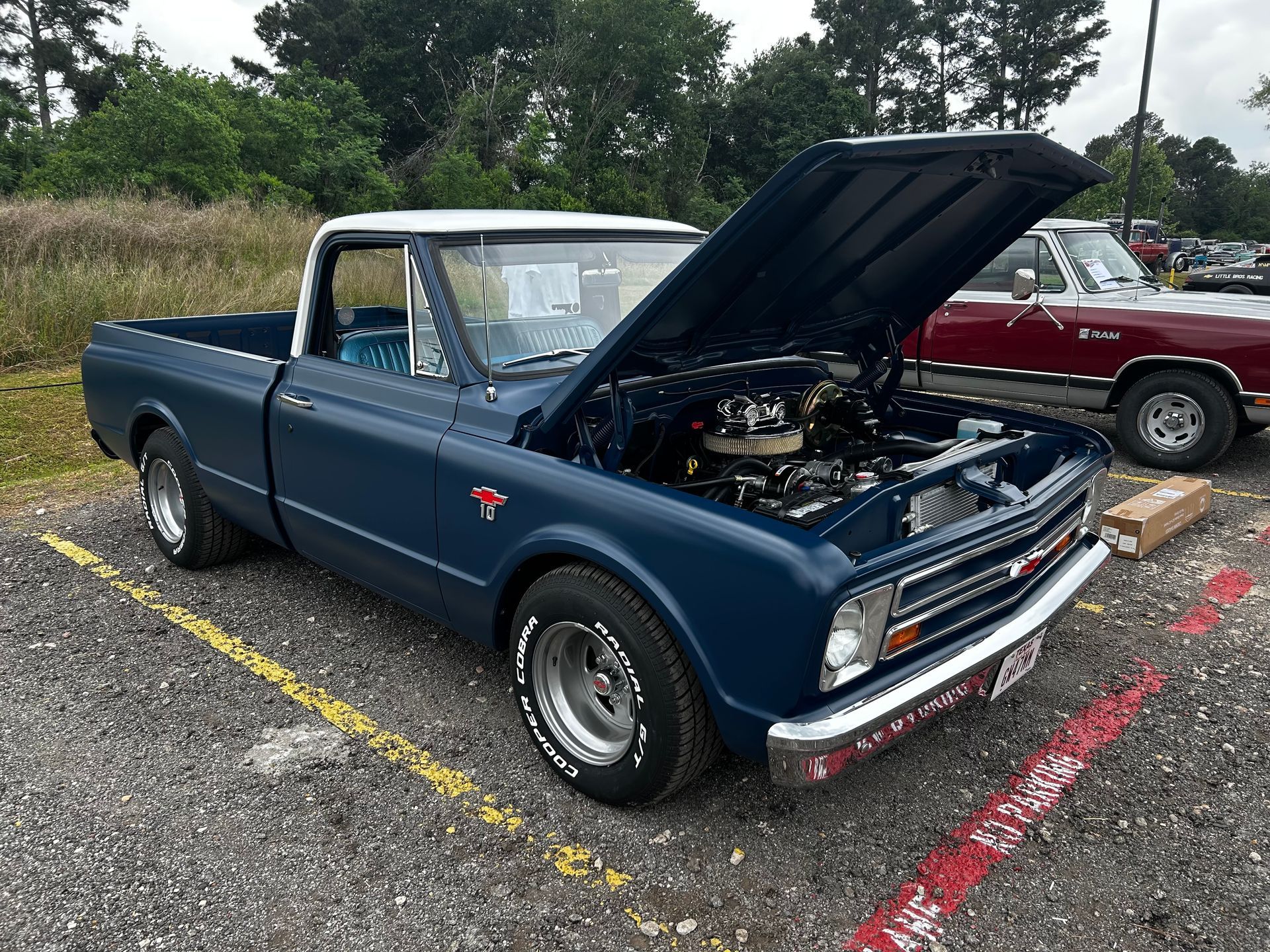 Dark blue classic Chevy pickup truck with white roof and hood open at an outdoor car show.
