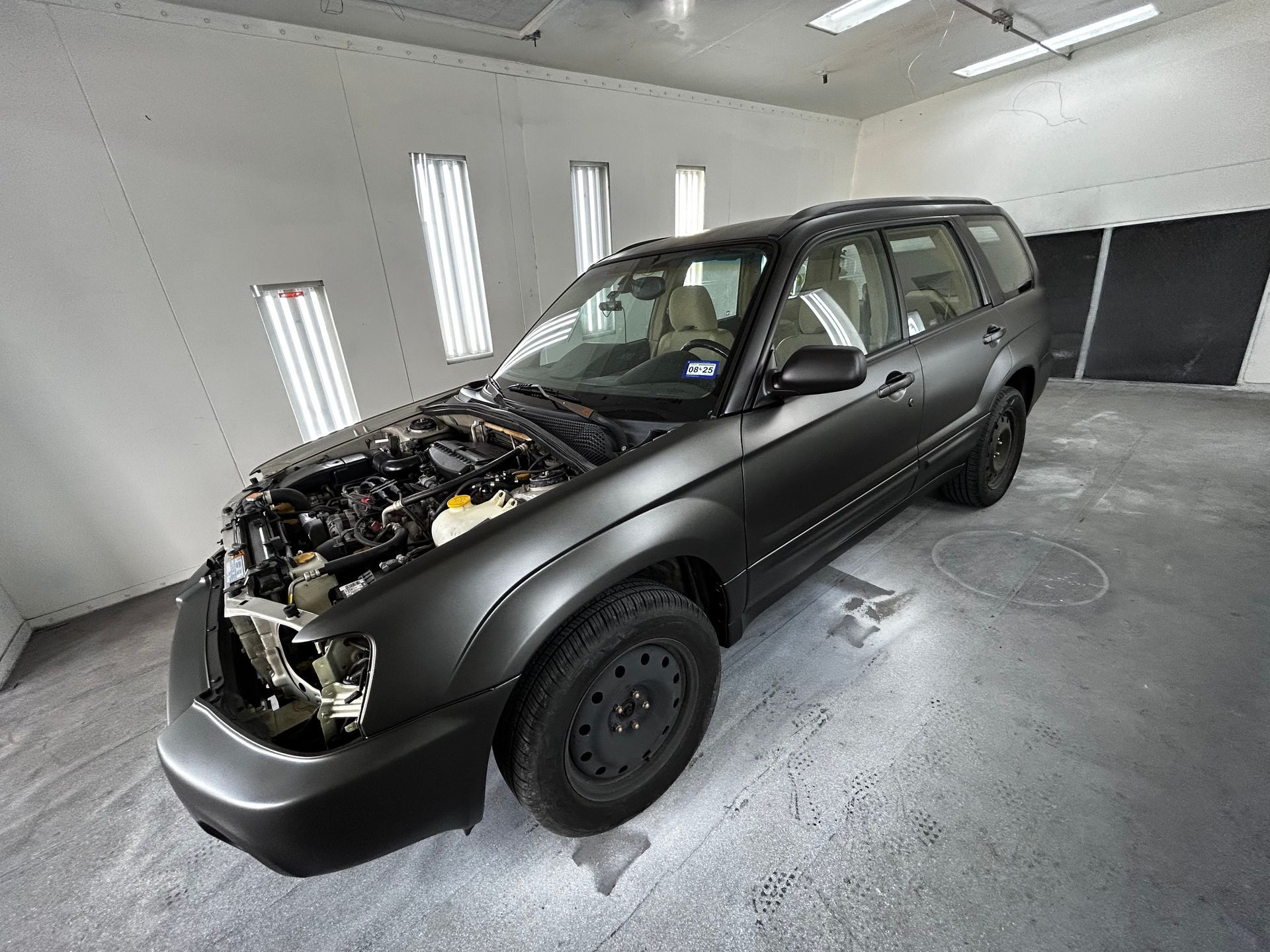 Black Subaru SUV in a paint booth, hood open.