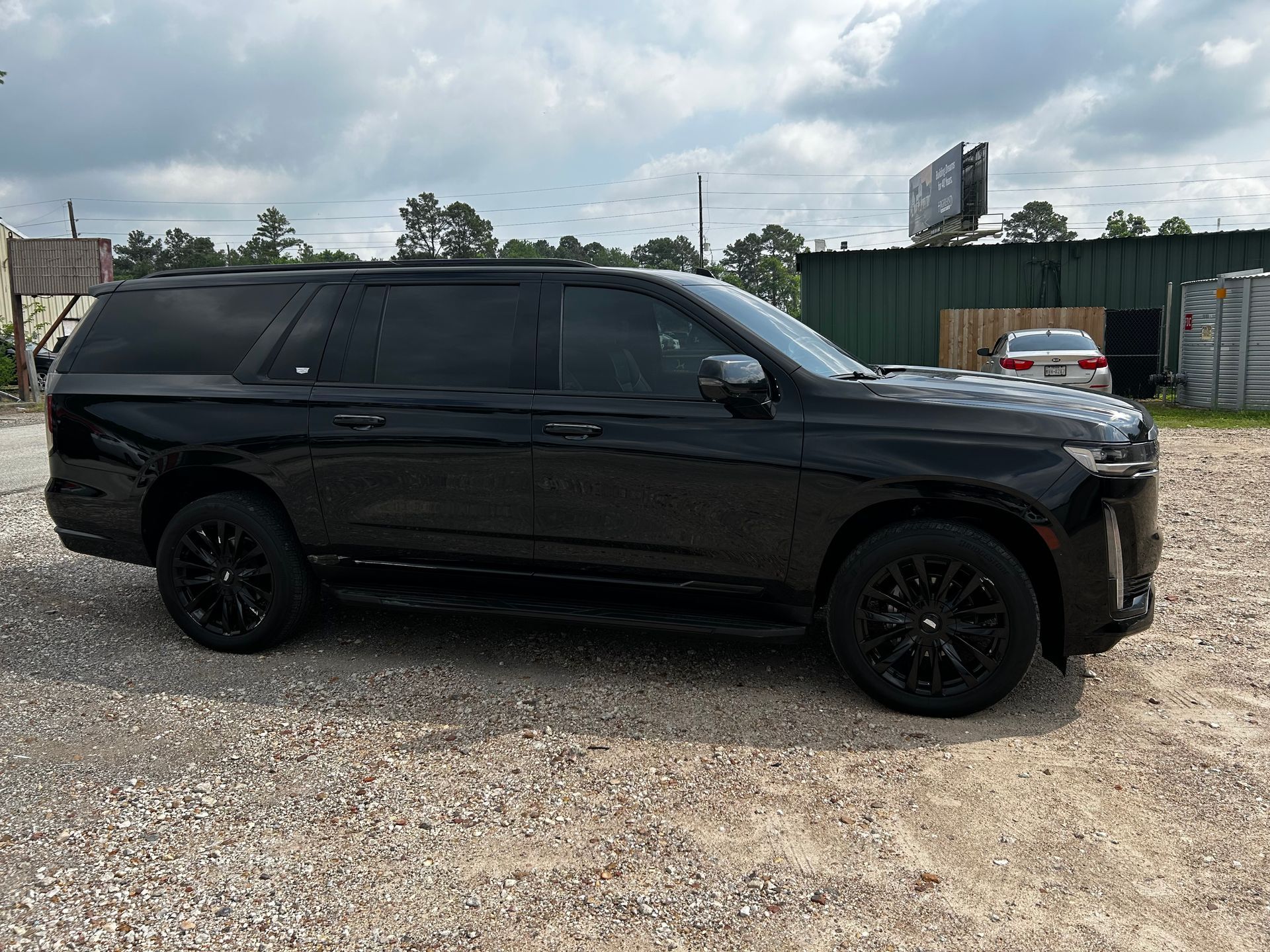 Black Cadillac Escalade SUV parked on gravel, side view.