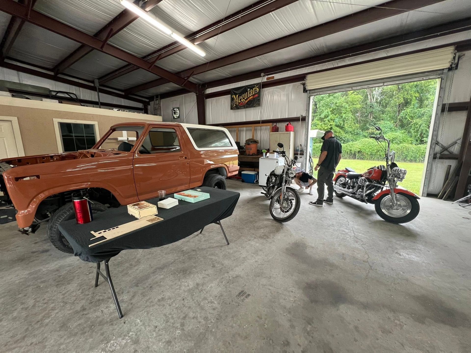 Garage with a brown Bronco, two motorcycles, and a person, with an open garage door.