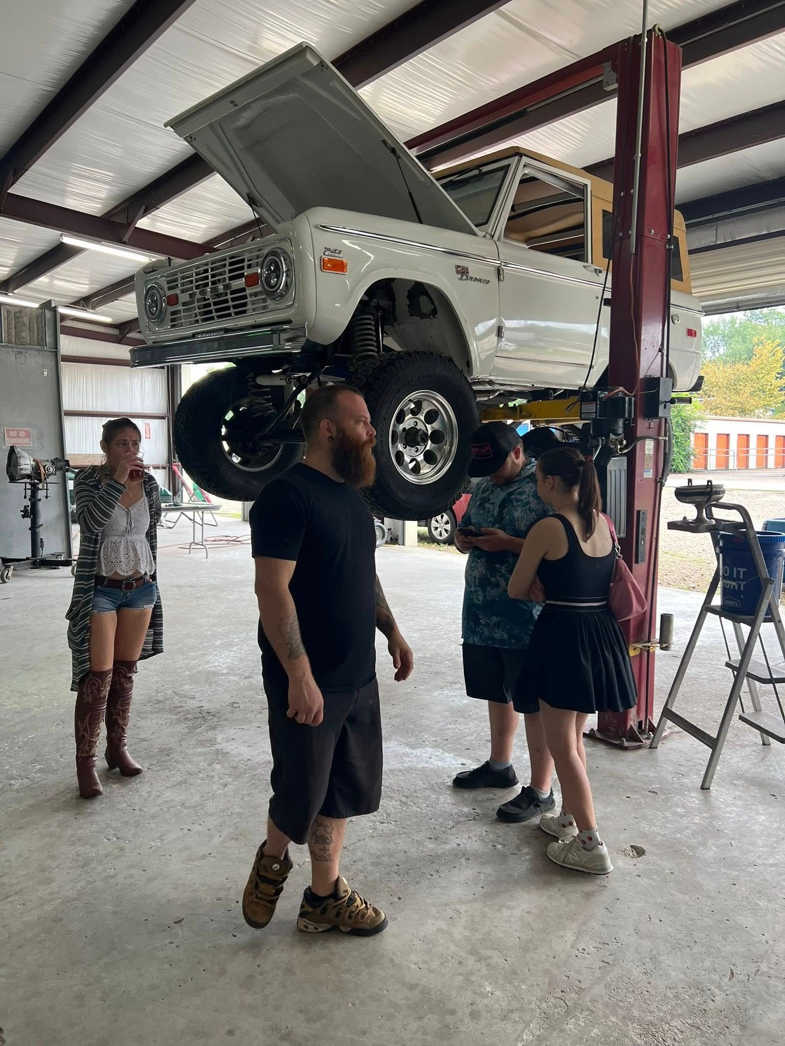 White Ford Bronco on a lift in a garage with people gathered around.
