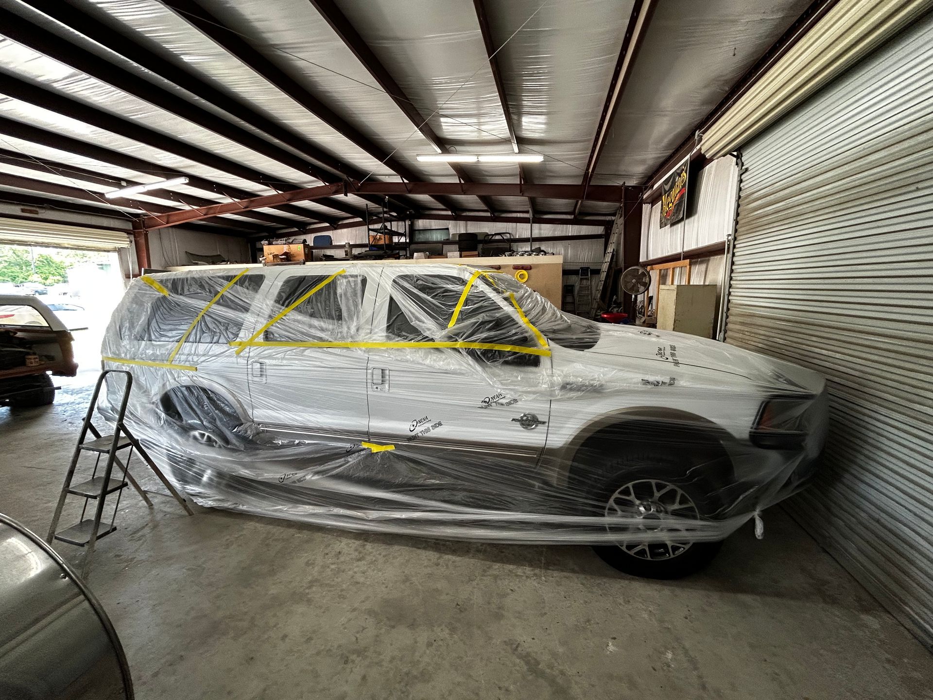 White SUV covered in plastic and tape inside a garage, ready for painting.