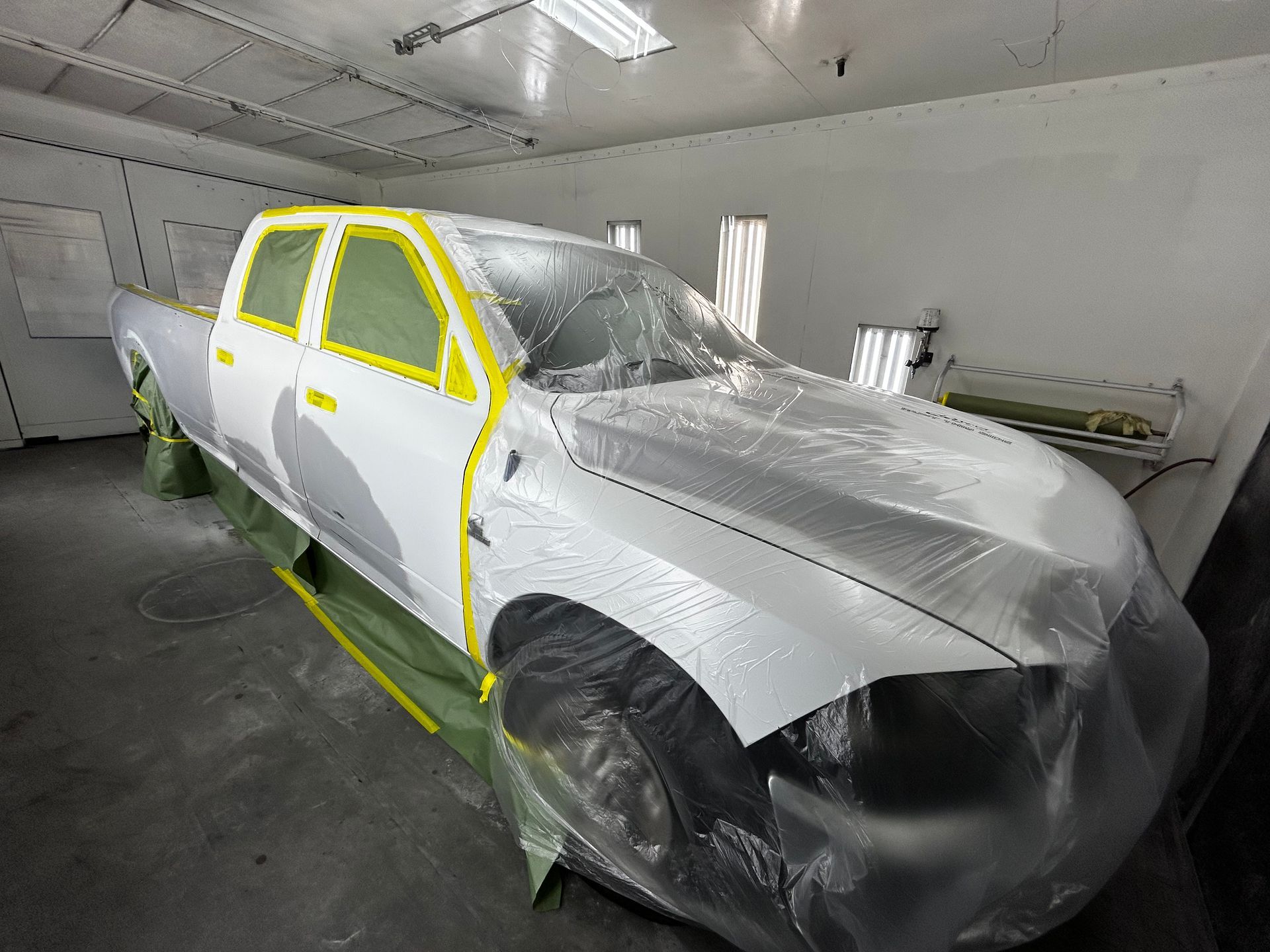White pickup truck masked for paint in a spray booth.