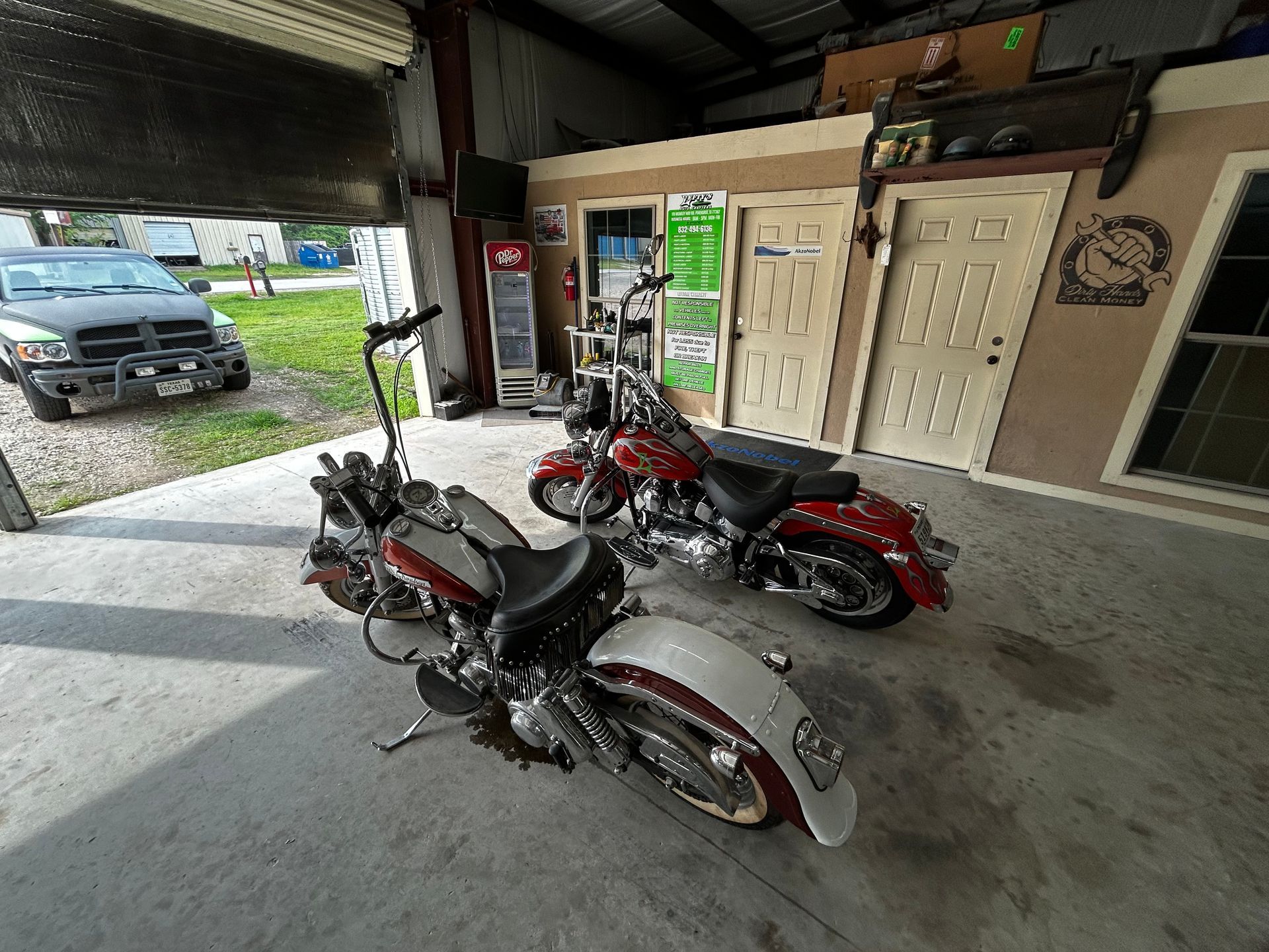 Two motorcycles parked inside a garage. One is red, the other silver. A black truck is visible outside.