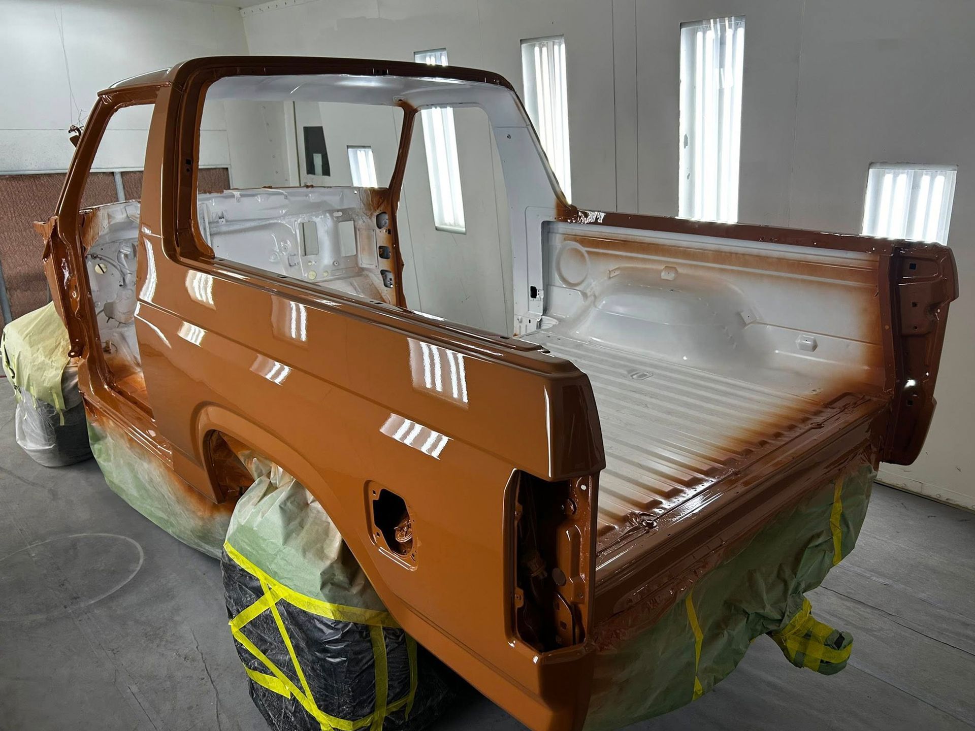 Orange Ford truck cab and bed in a spray paint booth; partial paint coverage.