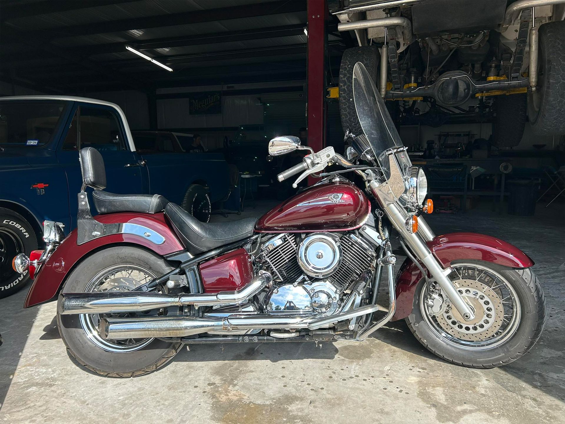 Maroon Yamaha motorcycle parked in a garage with a blue vehicle in the background.