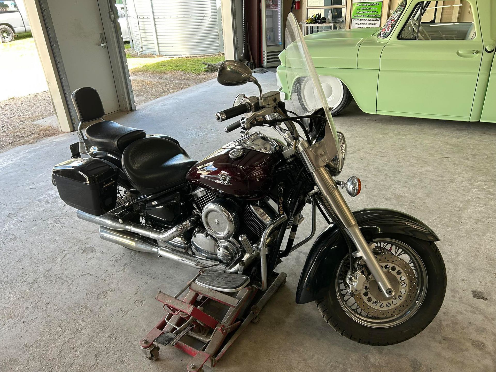 Dark red and black motorcycle on a lift in a garage, next to a light green truck.