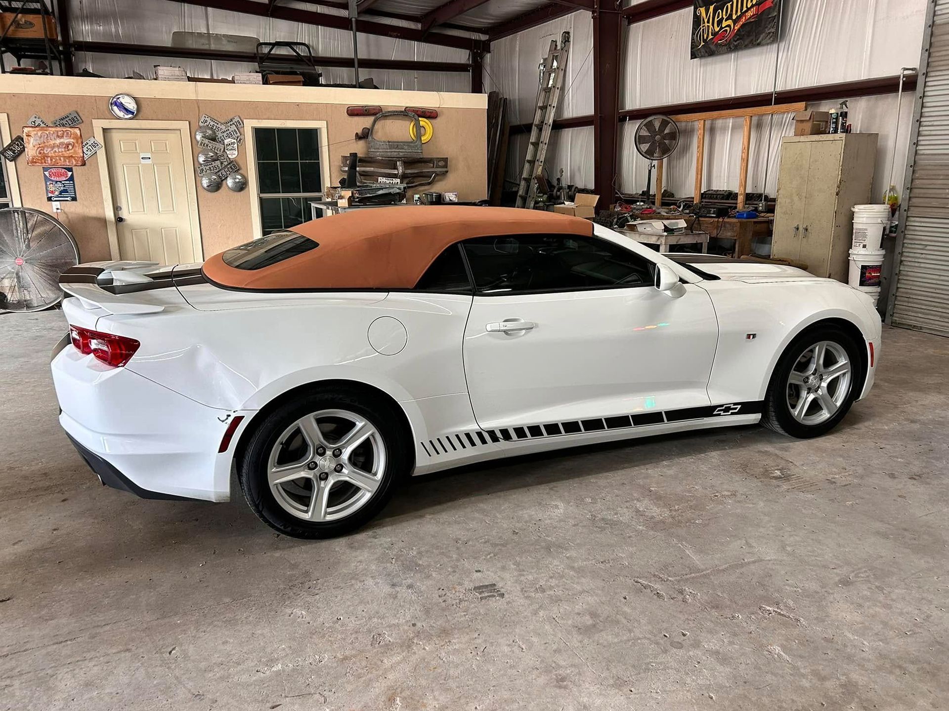 White convertible Camaro with tan top, parked in a garage.