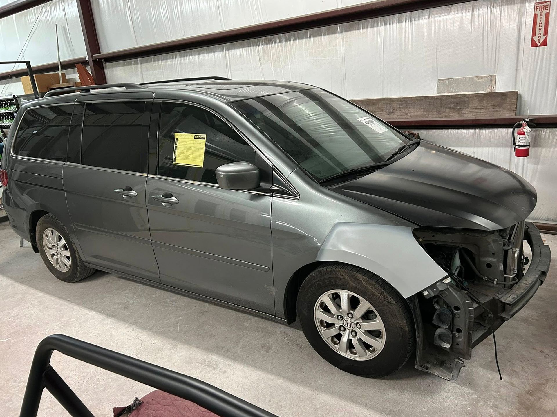 Gray minivan with front-end damage in a repair shop.