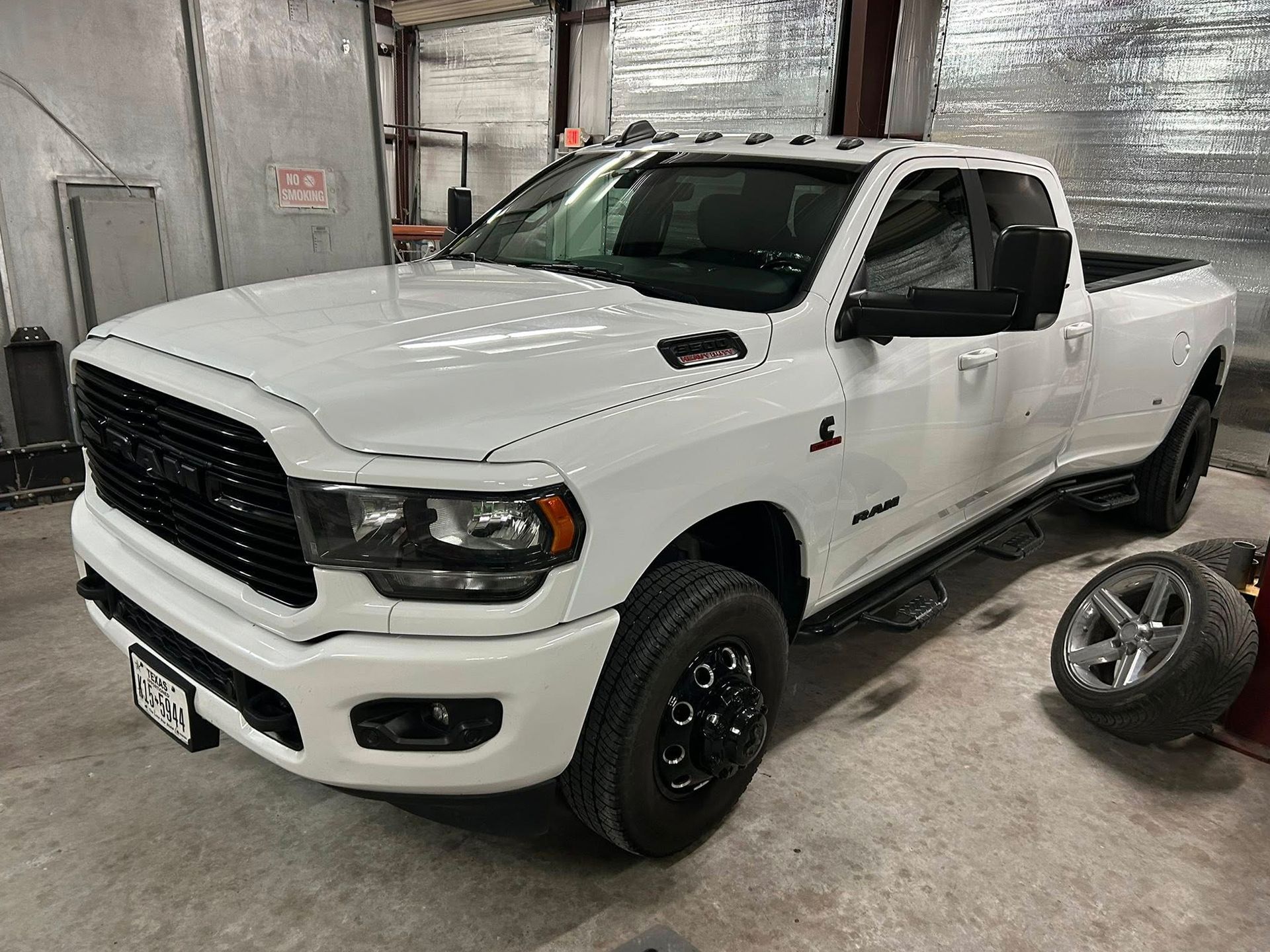White Ram 3500 pickup truck with black accents parked inside a garage, a spare tire to the right.