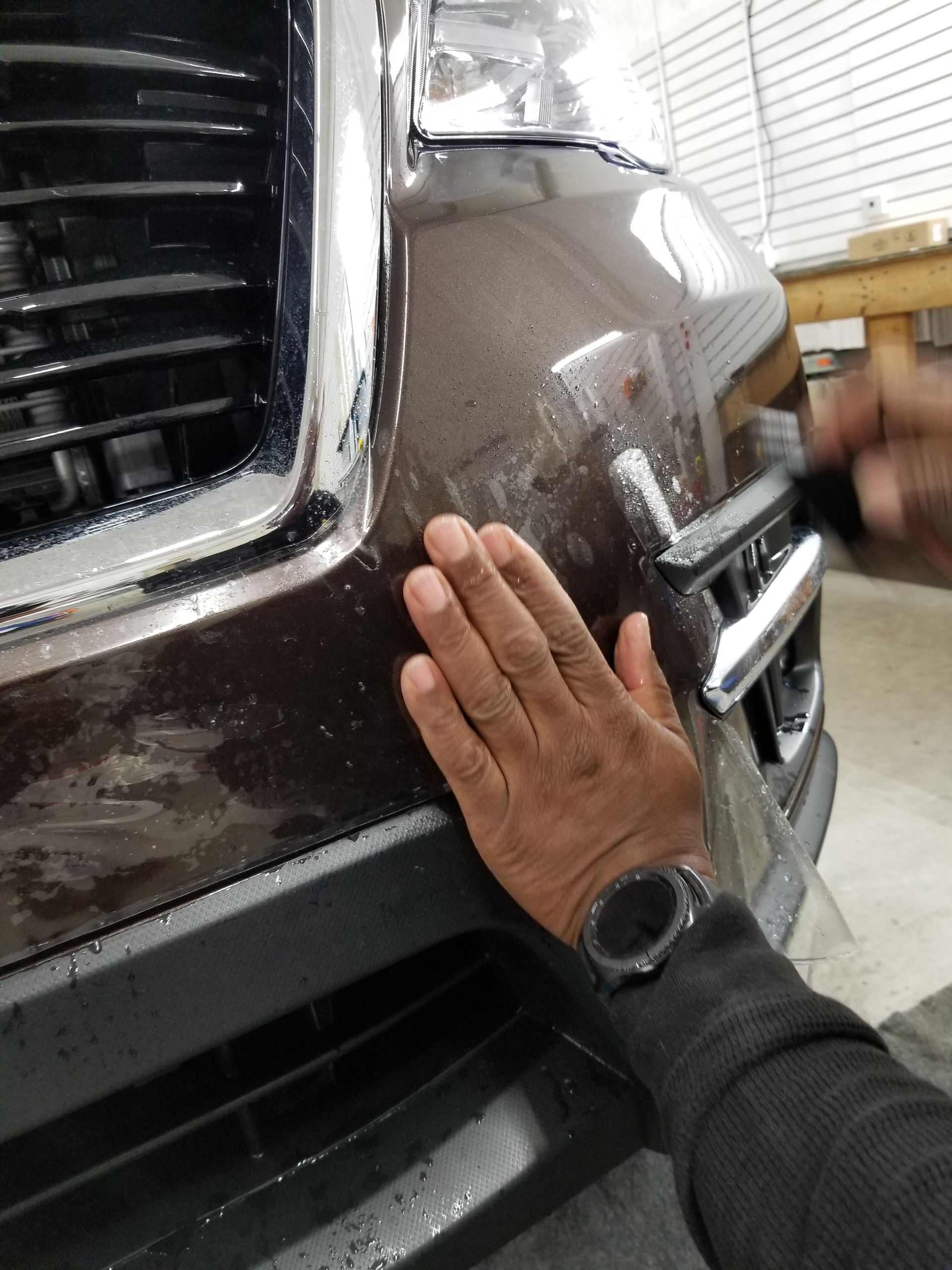 Person applying protective film to a brown car bumper.