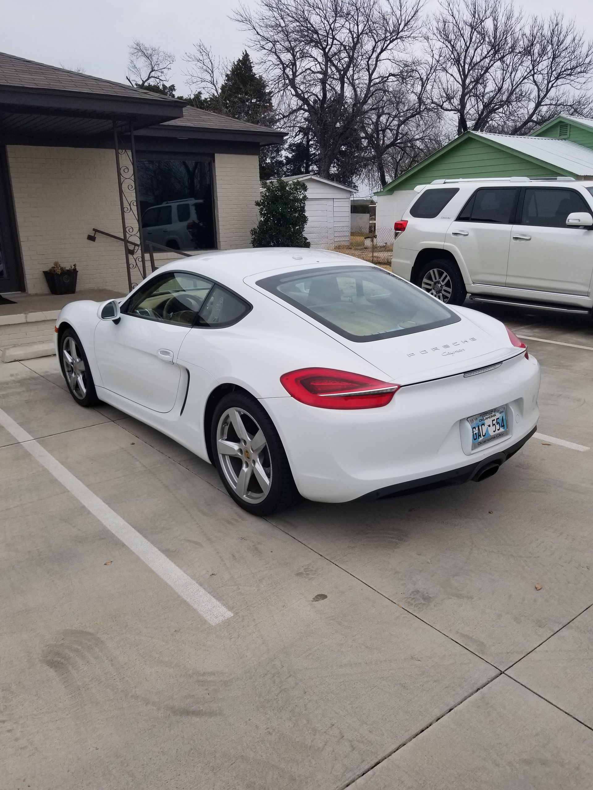 White Porsche coupe parked in front of a building, overcast day.