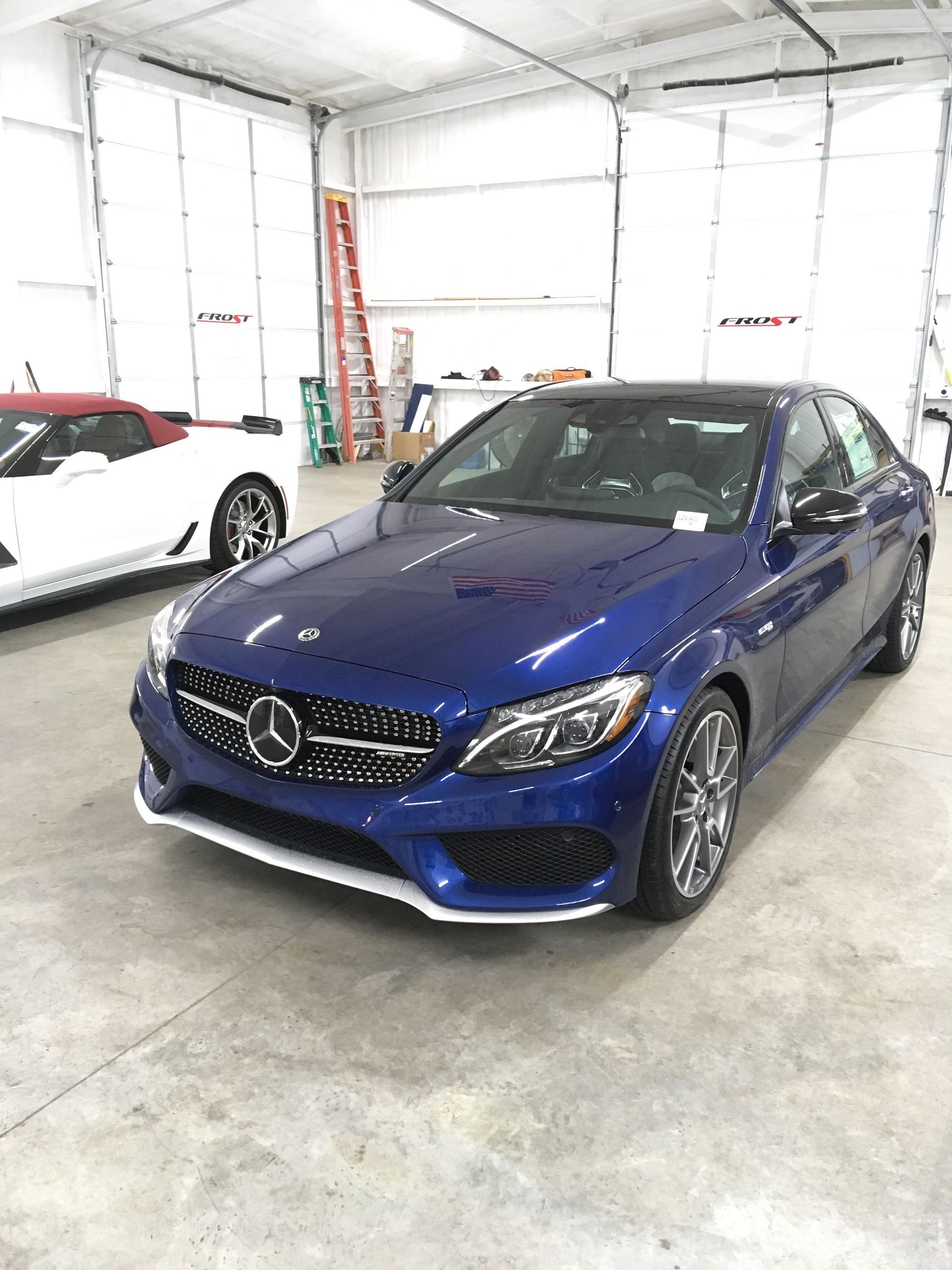 Blue Mercedes-Benz coupe in a garage; a white convertible is partially visible in the background.