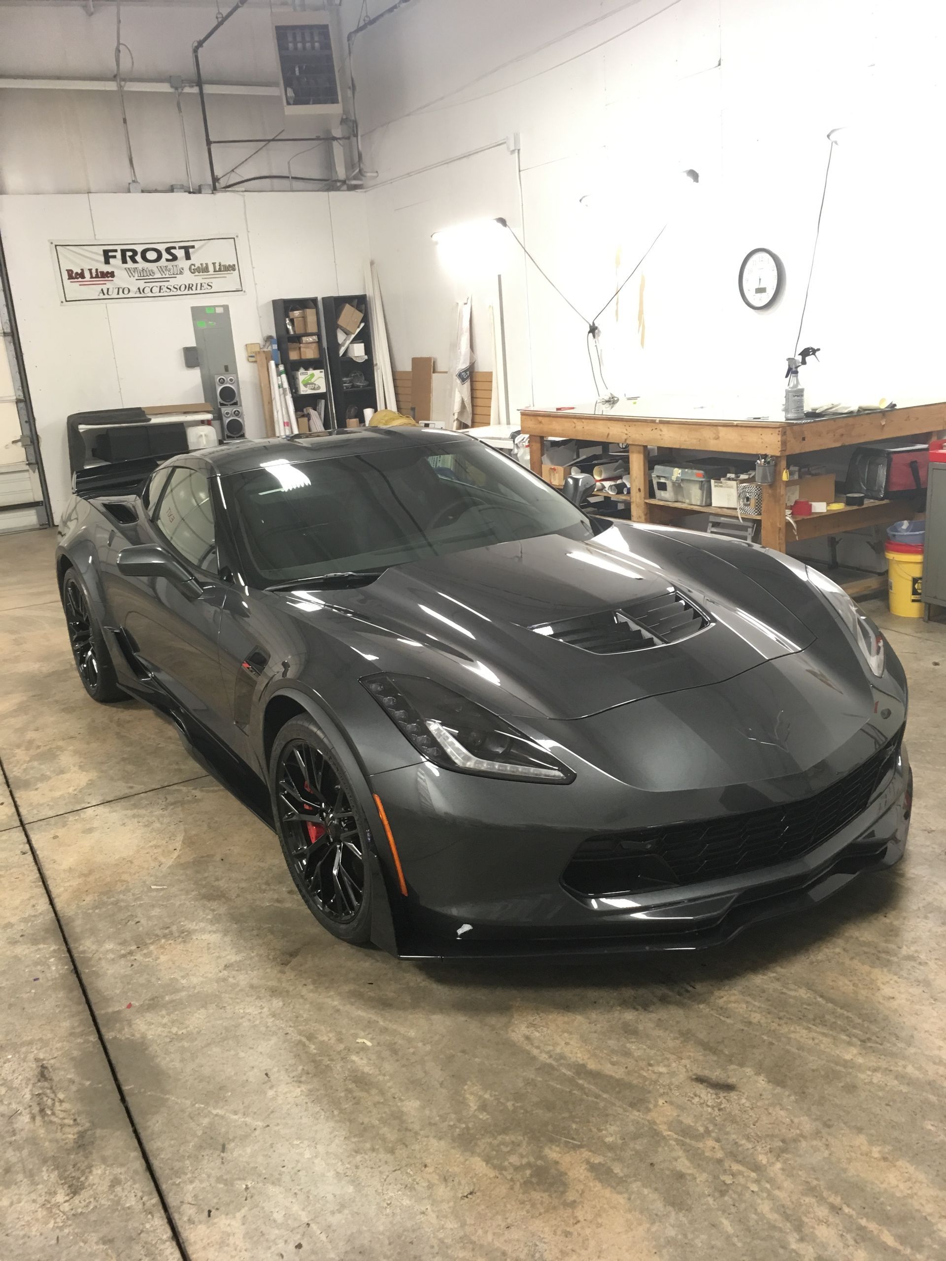 Dark gray sports car inside a garage with work benches and a sign.