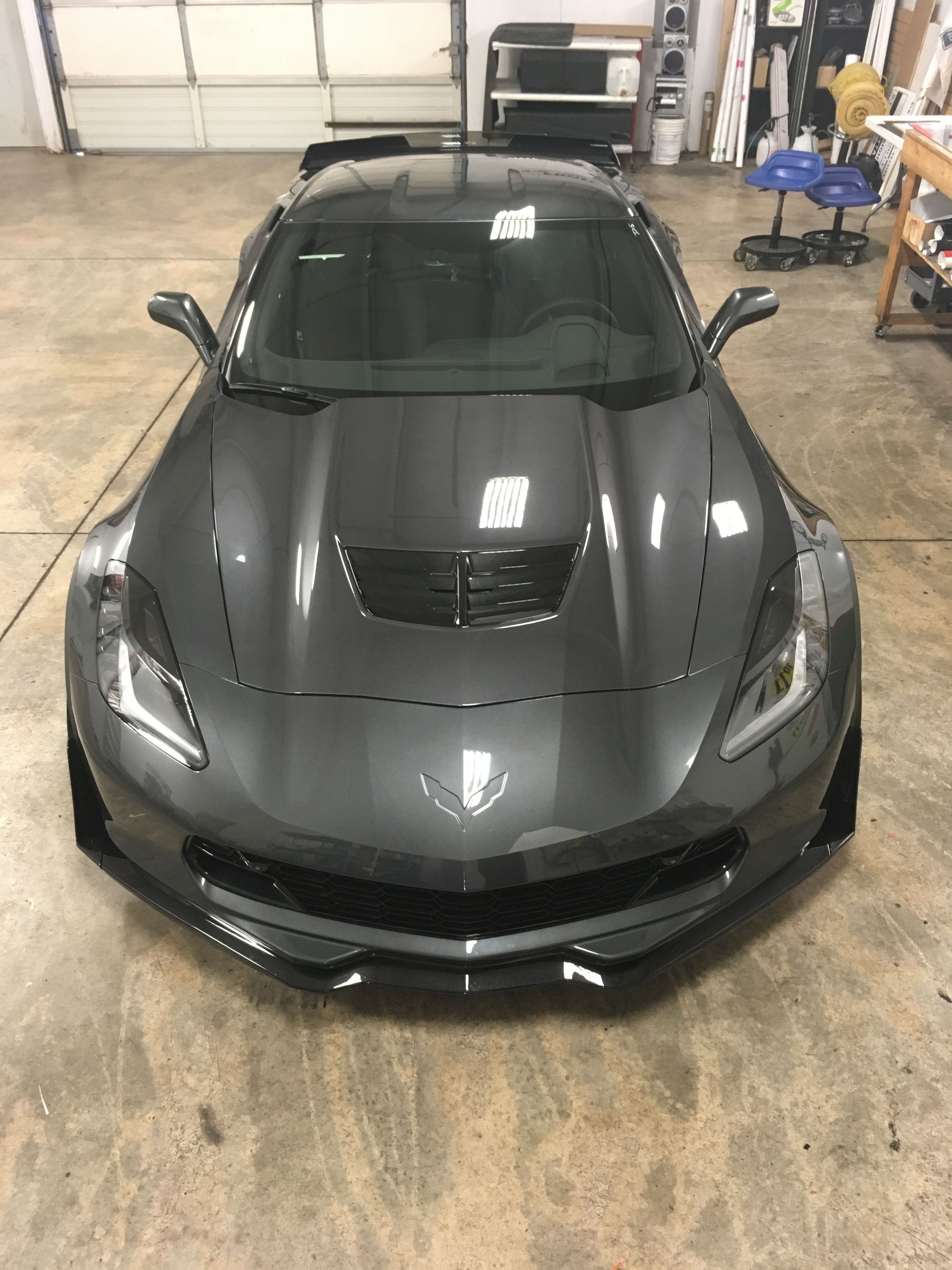 Gray sports car in a garage, angled slightly. Hood scoop, spoiler, and front splitter are visible.