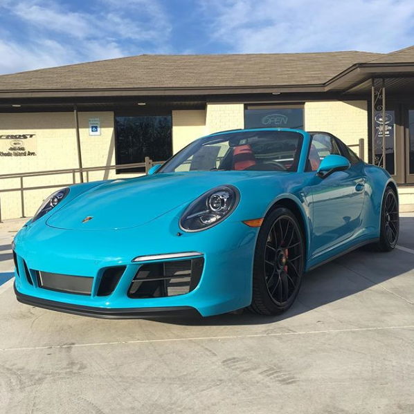 Bright blue Porsche Targa parked in front of a beige building, with black wheels and red interior.
