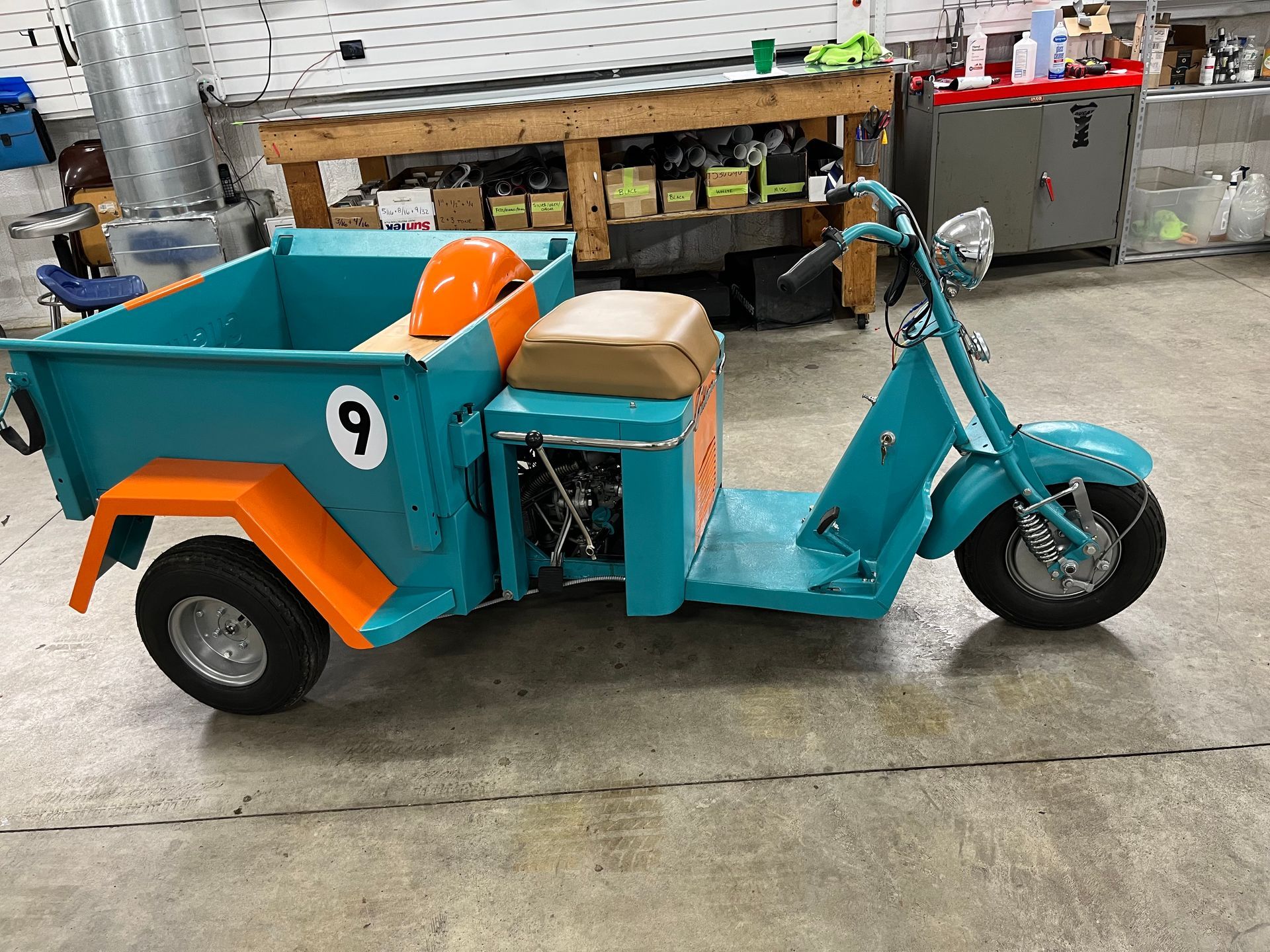 Teal and orange vintage utility scooter with a cargo bed, parked in a workshop.