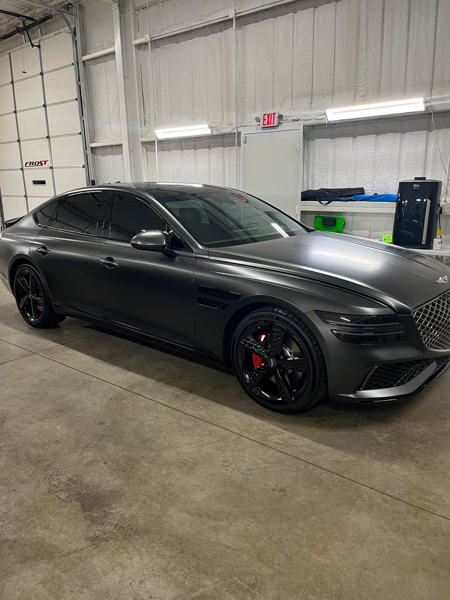 Dark gray sedan with tinted windows inside a garage. Black wheels, red brake calipers.