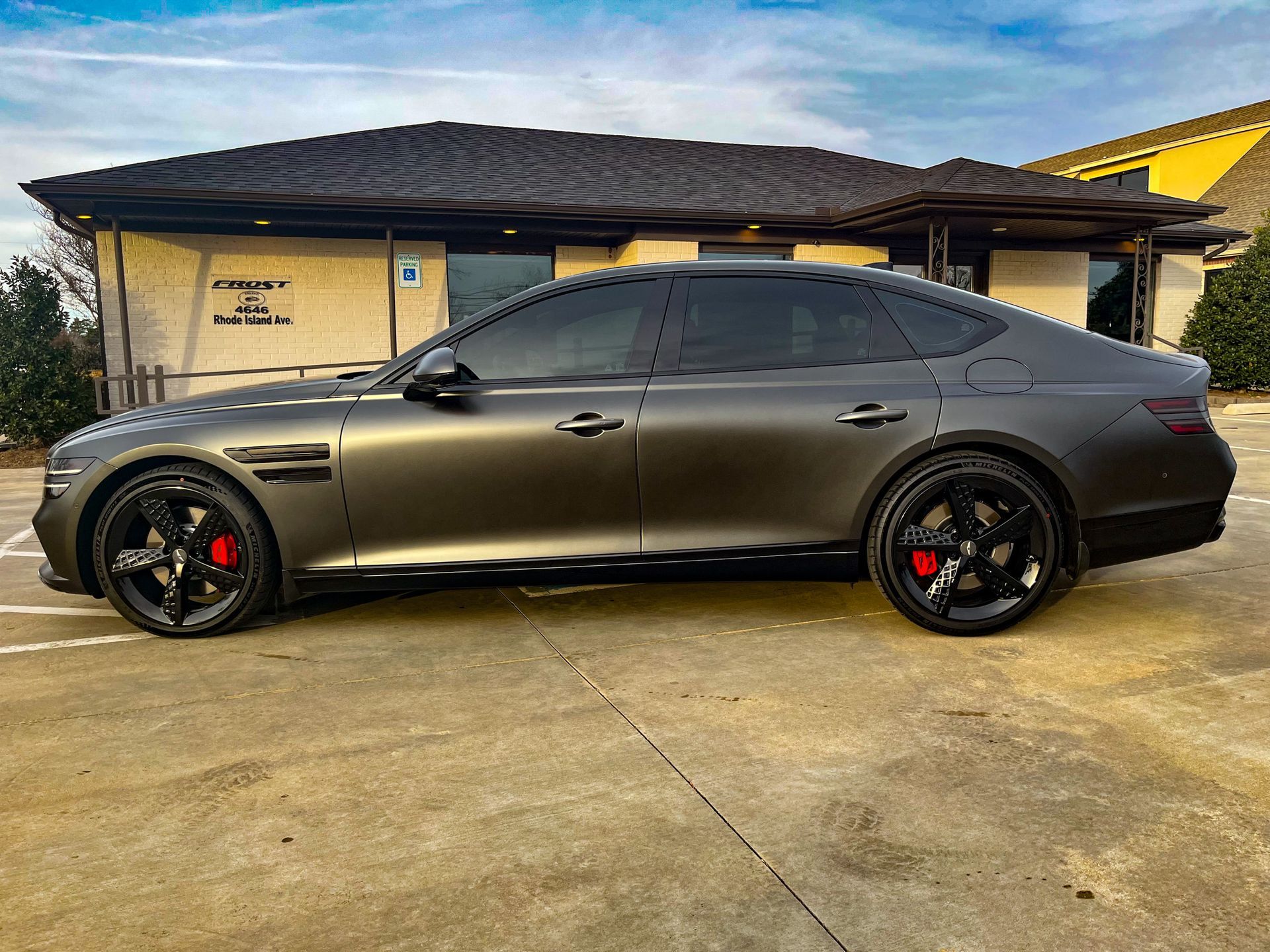 Gray luxury sedan with black wheels and red brake calipers parked in front of a building.