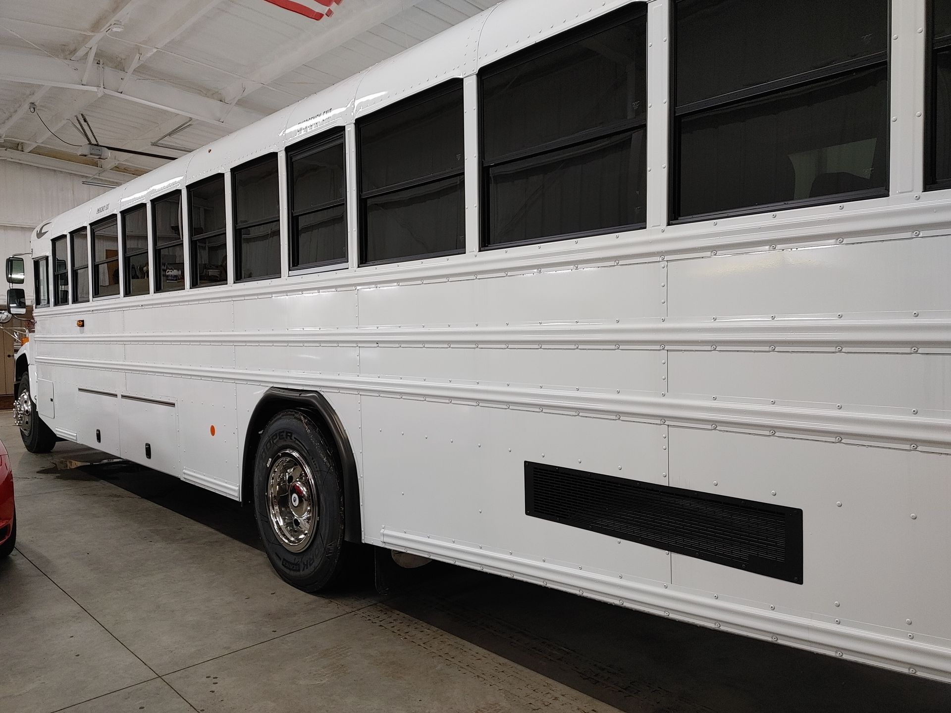 White bus parked indoors, featuring rows of windows and a large black vent.