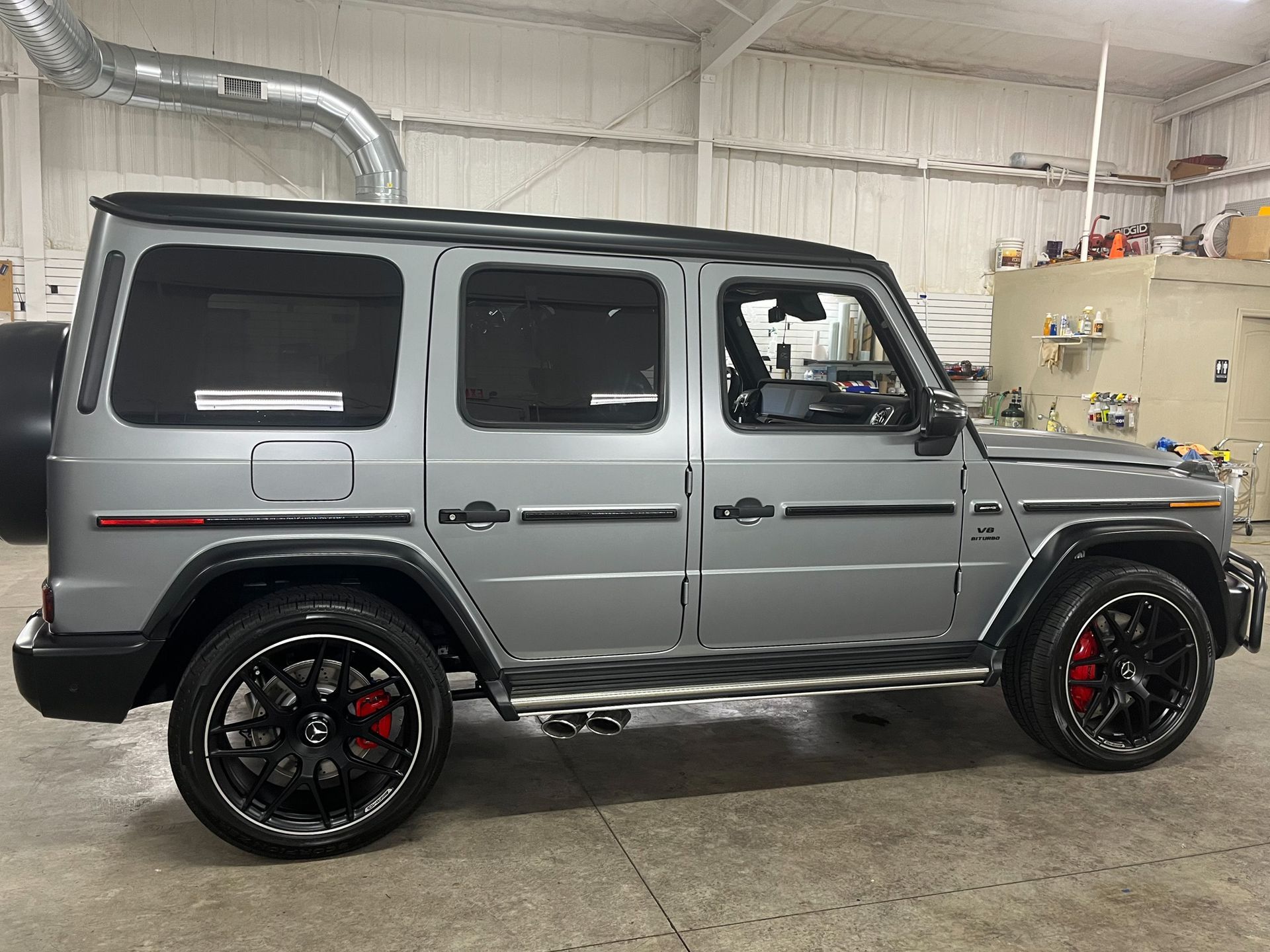 Silver Mercedes-Benz G-Class SUV with black accents, large black wheels, red brake calipers, parked indoors.