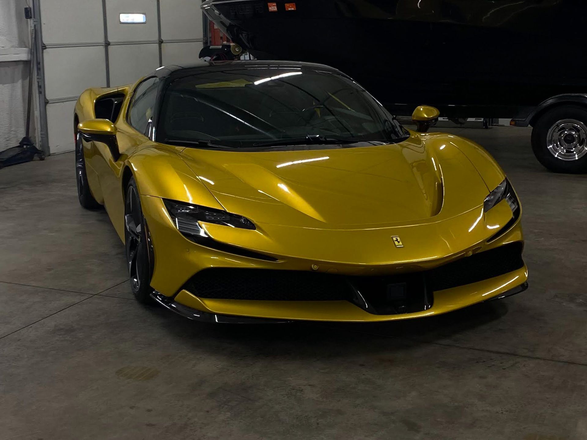 Yellow Ferrari SF90 in a garage, with a black roof, and a black car behind it.