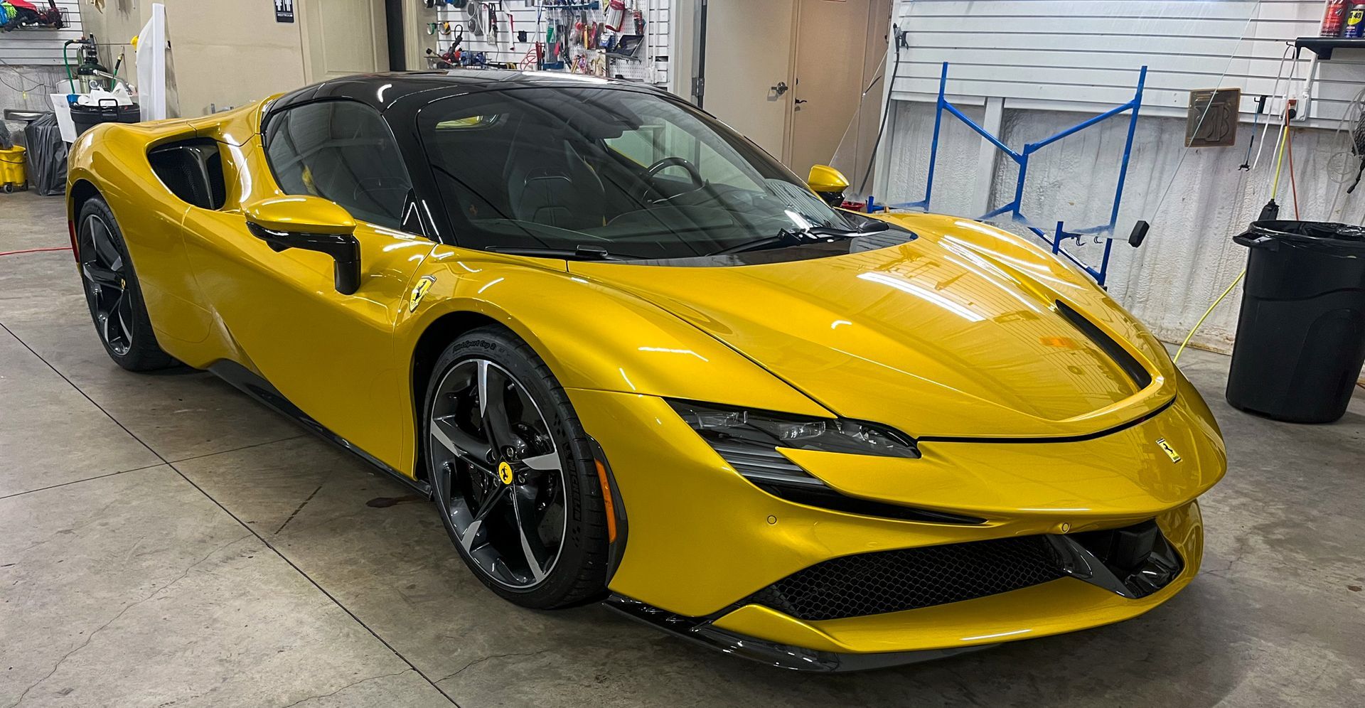 Yellow Ferrari SF90 sports car inside a garage with black wheels and roof.
