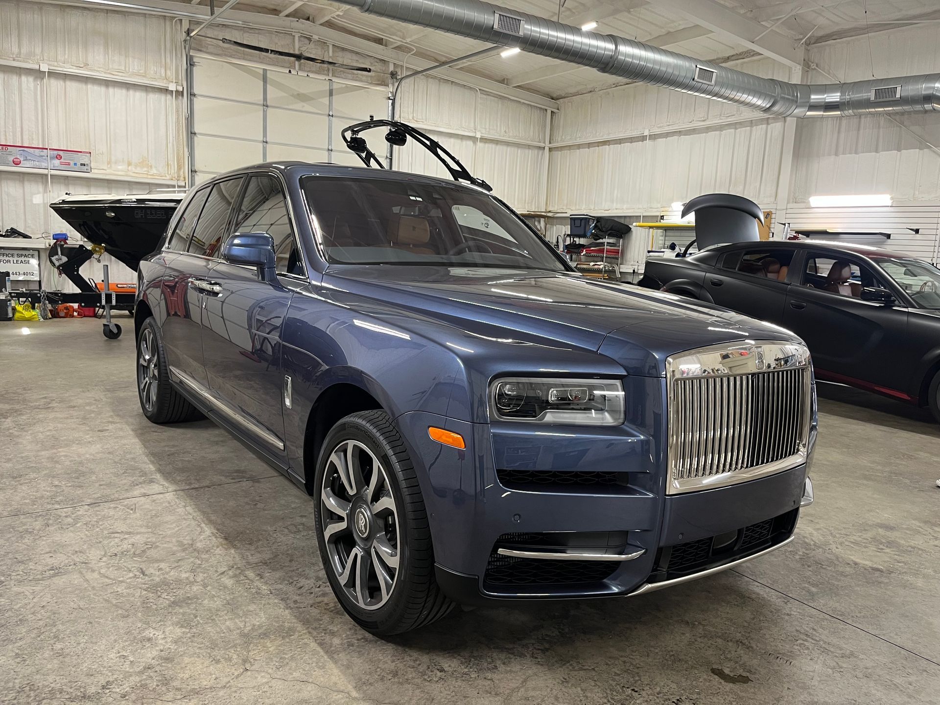 Blue Rolls-Royce Cullinan SUV parked in a shop. A black car is partially visible in the background.