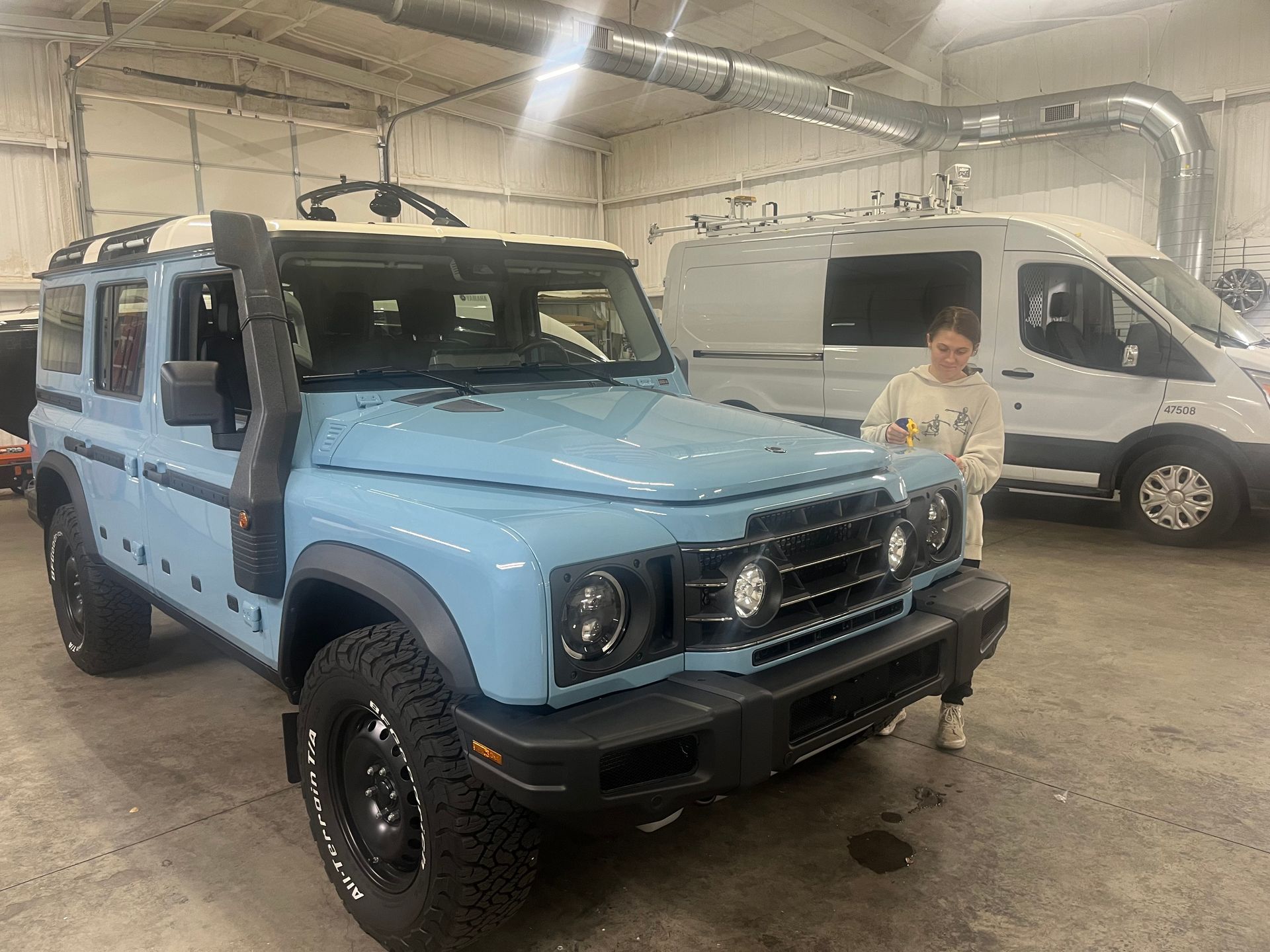 Light blue off-road vehicle with snorkel parked in a garage, person standing nearby.