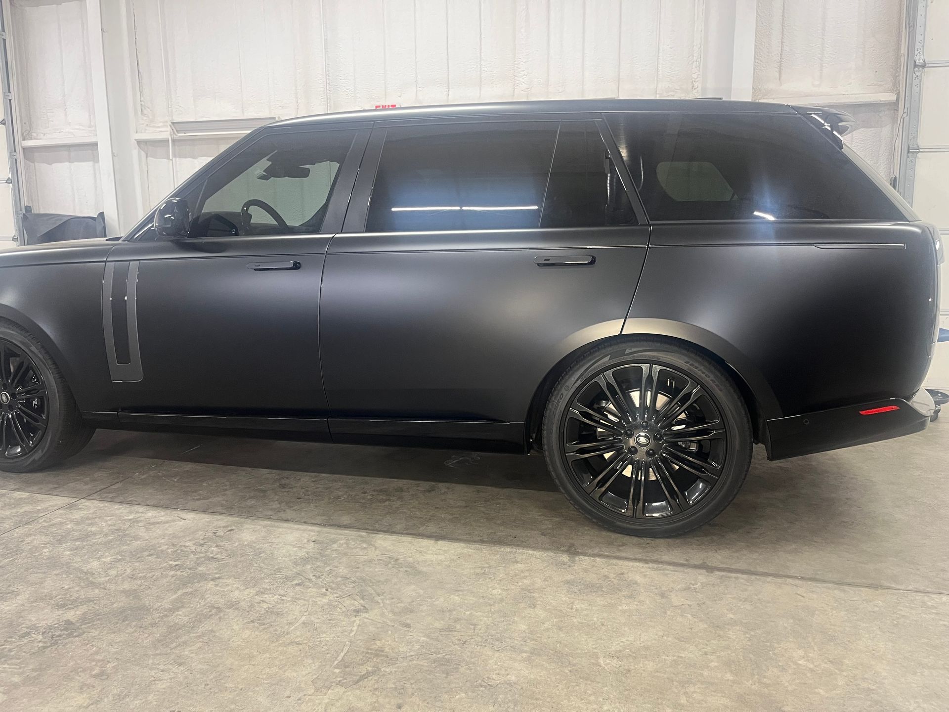 Black matte Range Rover SUV, black tinted windows, black wheels, in a garage.