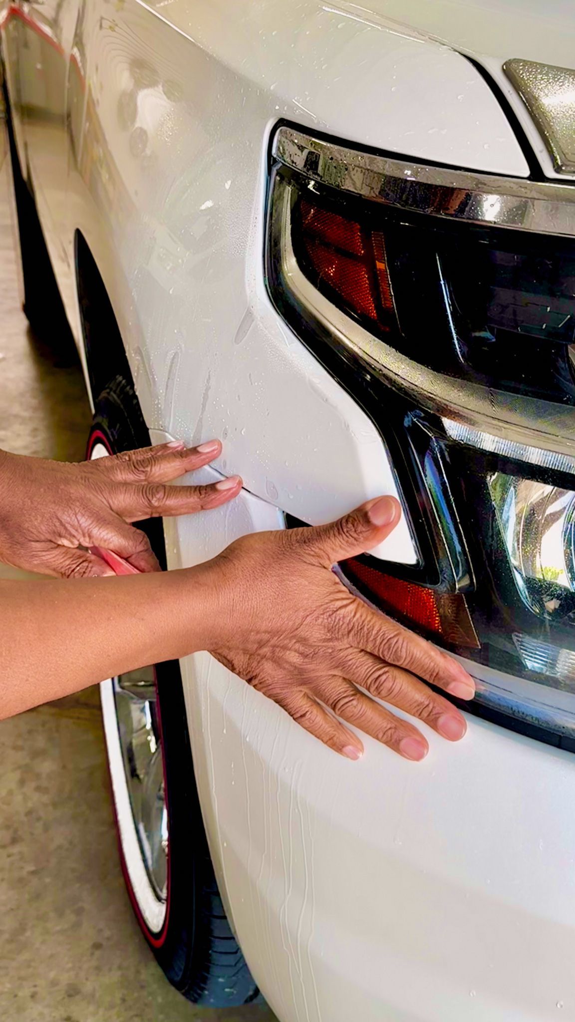 Hands smoothing white film on a white car bumper, near the headlight.