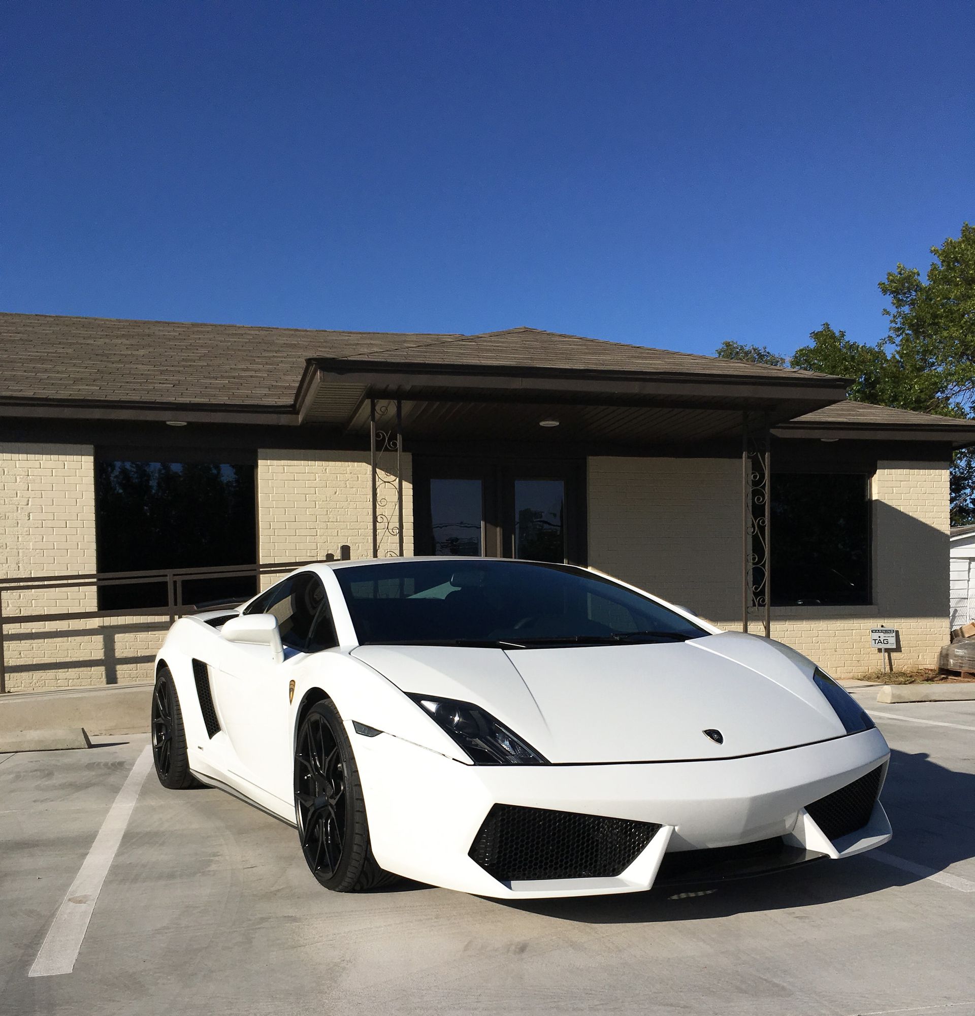 White Lamborghini sports car parked in front of a low building on a sunny day.