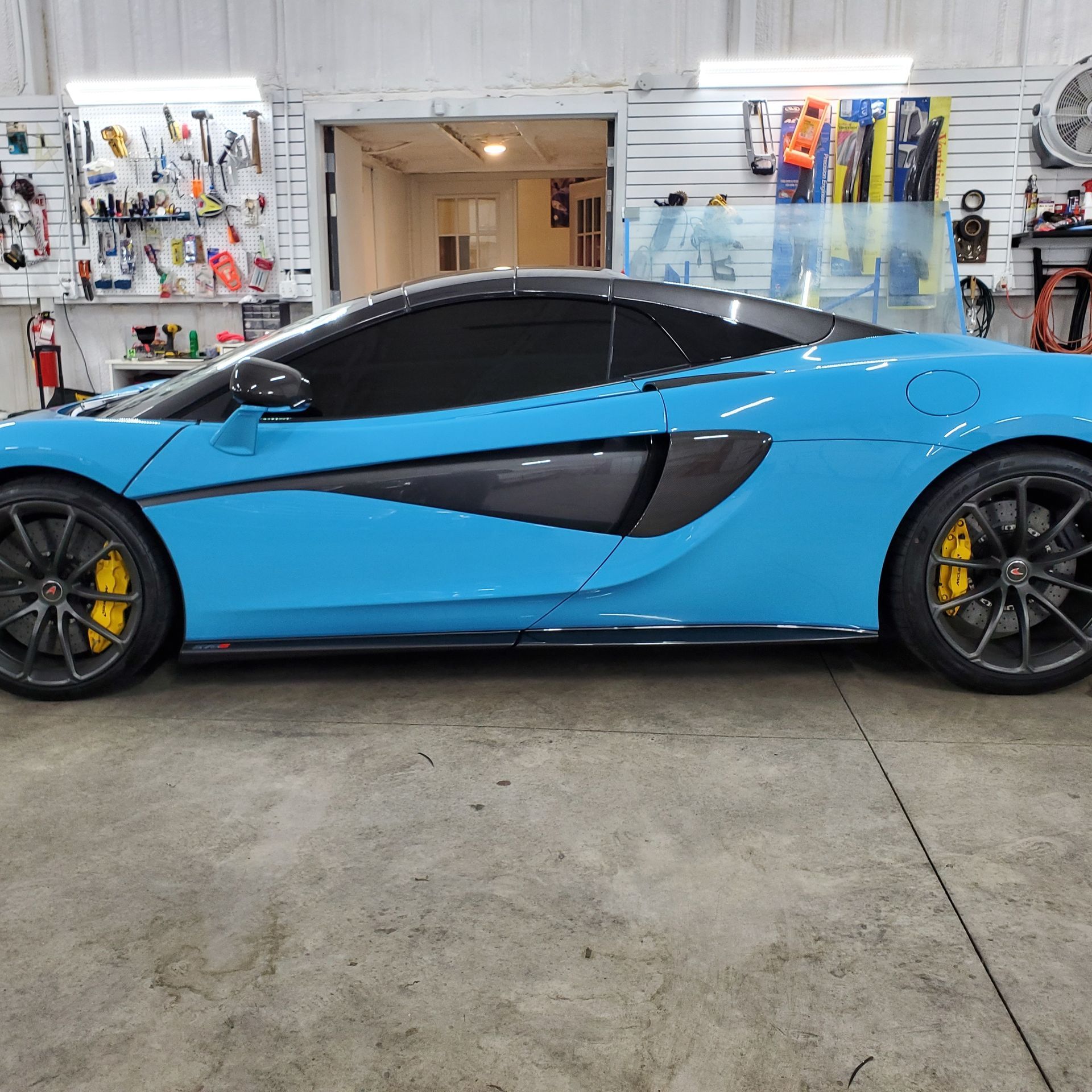 Blue McLaren sports car with tinted windows and yellow brake calipers in a garage.