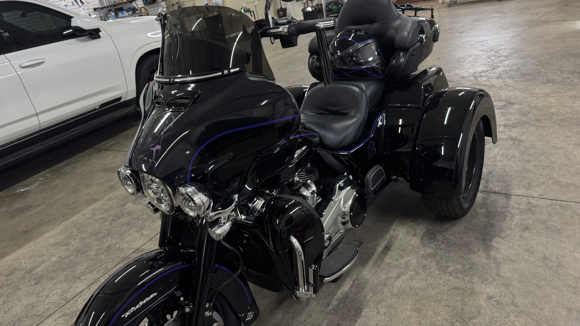 Black trike motorcycle with windshield, chrome accents, parked indoors.