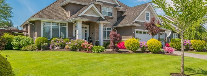 A large house with a lush green lawn and flowers in front of it.