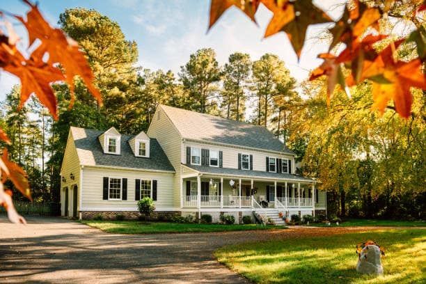 A large white house is surrounded by trees and leaves on a sunny day.