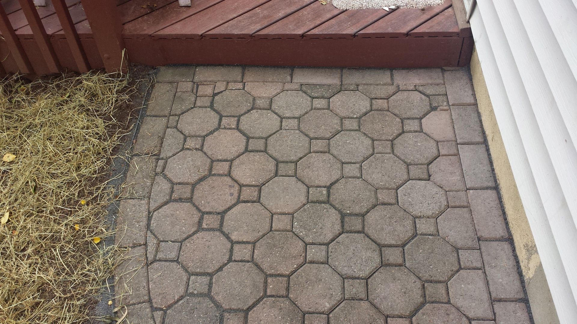 A brick walkway with a wooden deck in the background.